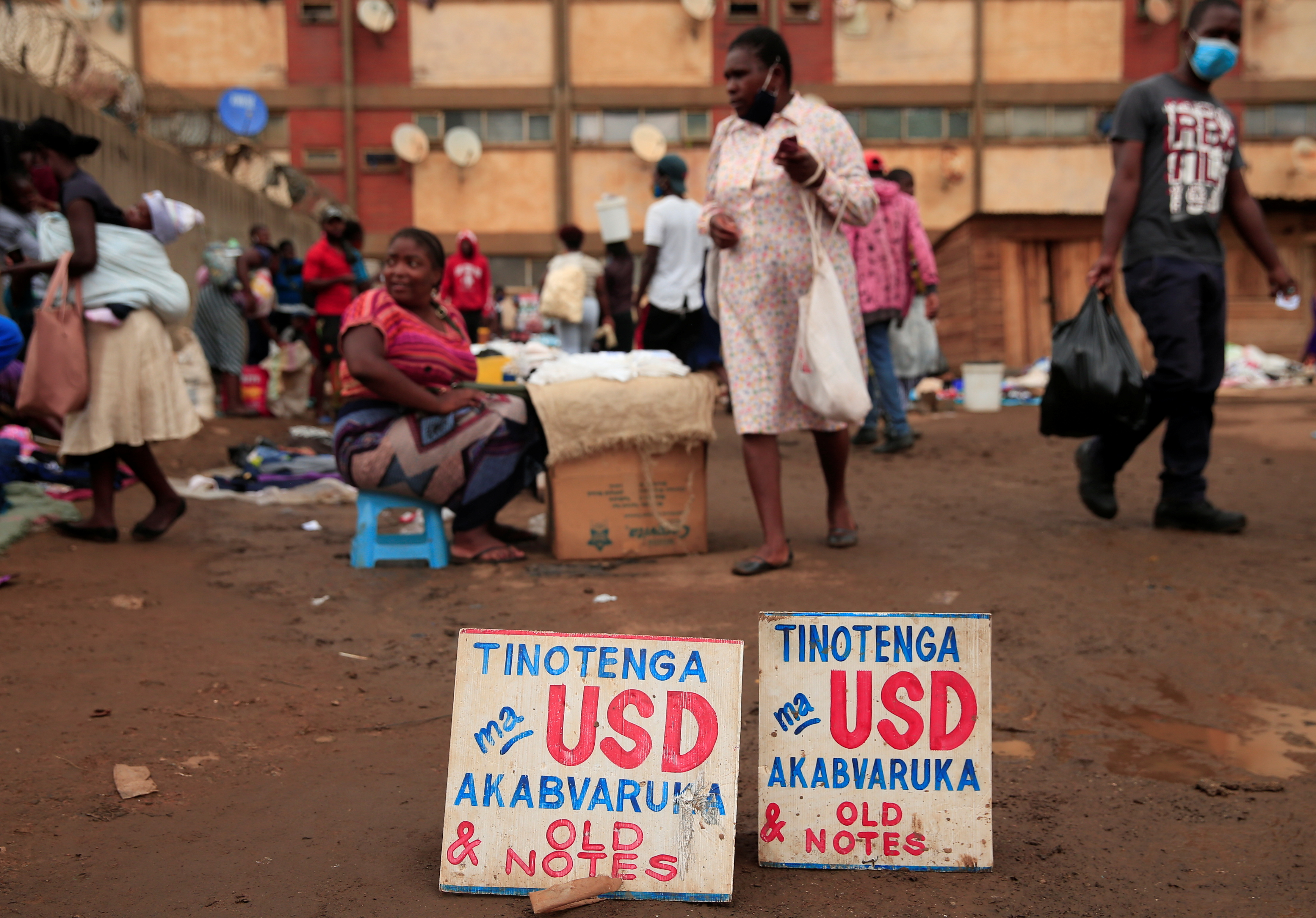 People walk past a money-changer’s sign at a market in Harare in 2020