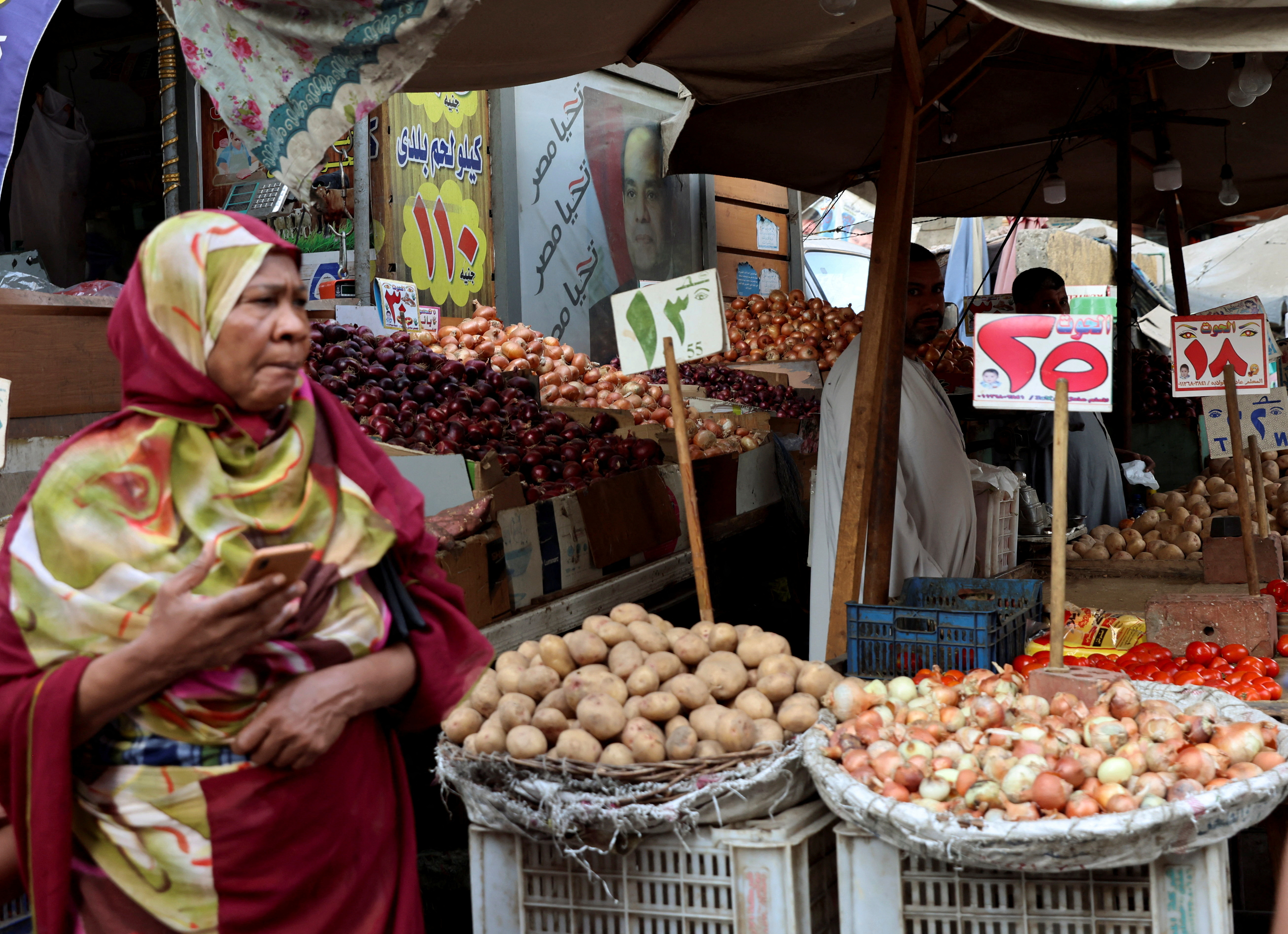 A vendor waits for customers beside a banner with an image of President Abdel Fattah el-Sisi, at a market in Cairo