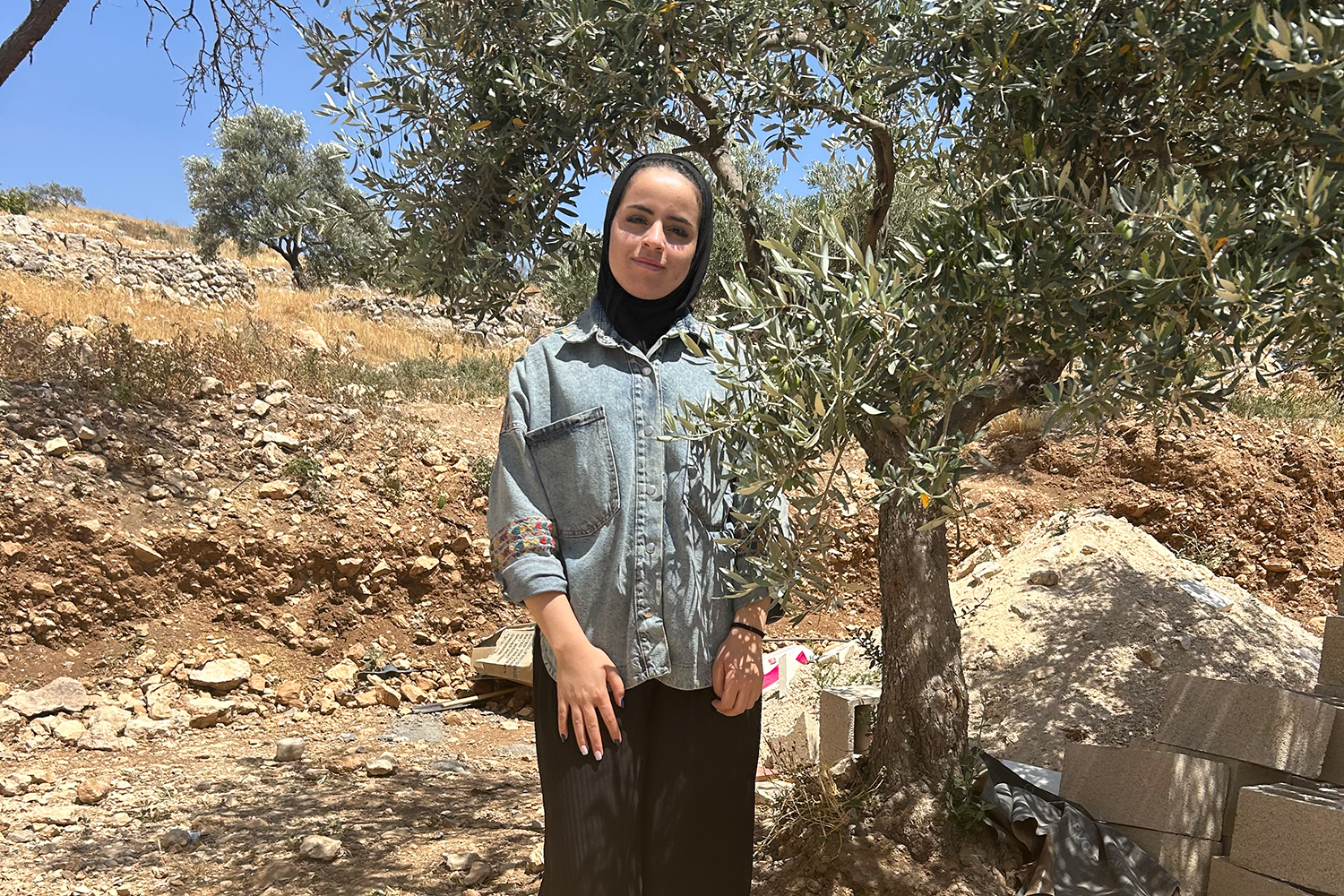 Sameeha Huriani standing beside an olive tree in her village, At-Tuwani.
