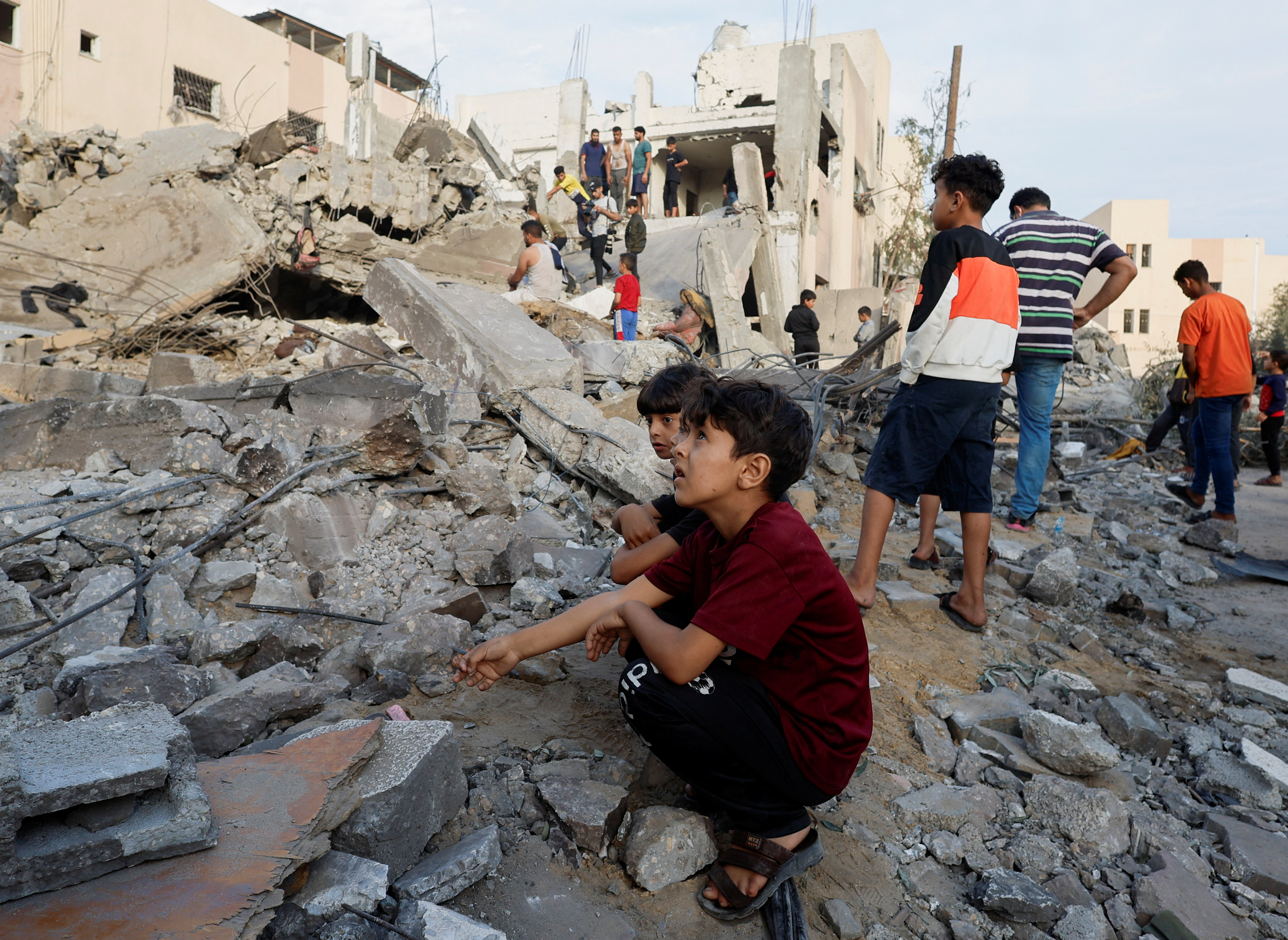 Palestinian children sit next destroyed building