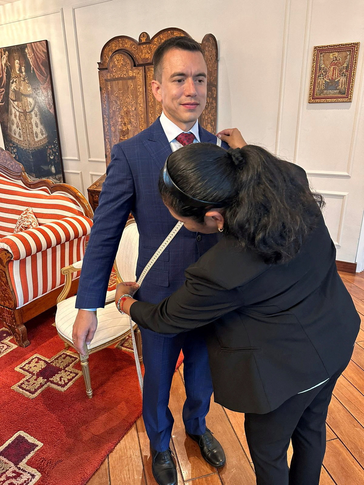 Daniel Noboa gets measured for his presidential sash in a room of the presidential palace. A tailor places a measuring tape across his chest.