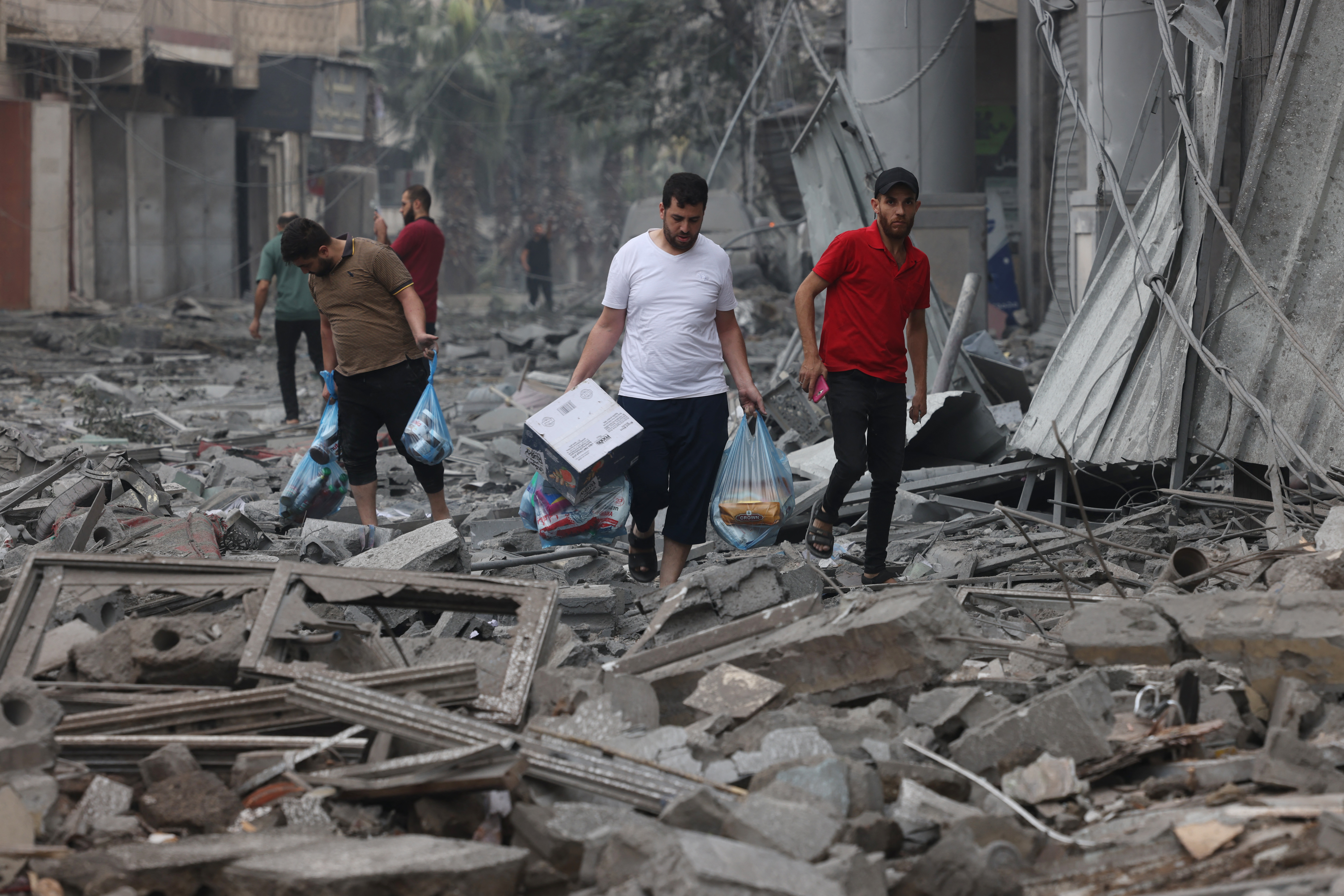 Palestinian men carry food supplies as they walk through debris