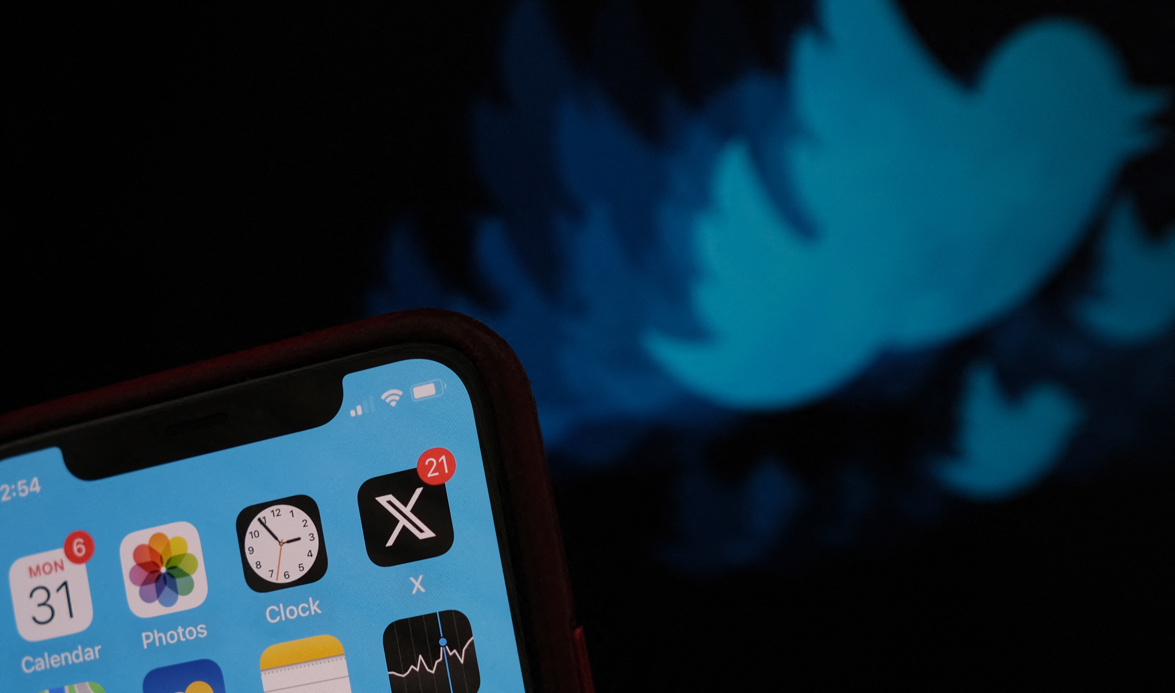 An X app on a phone with the Twitter bird logo behind