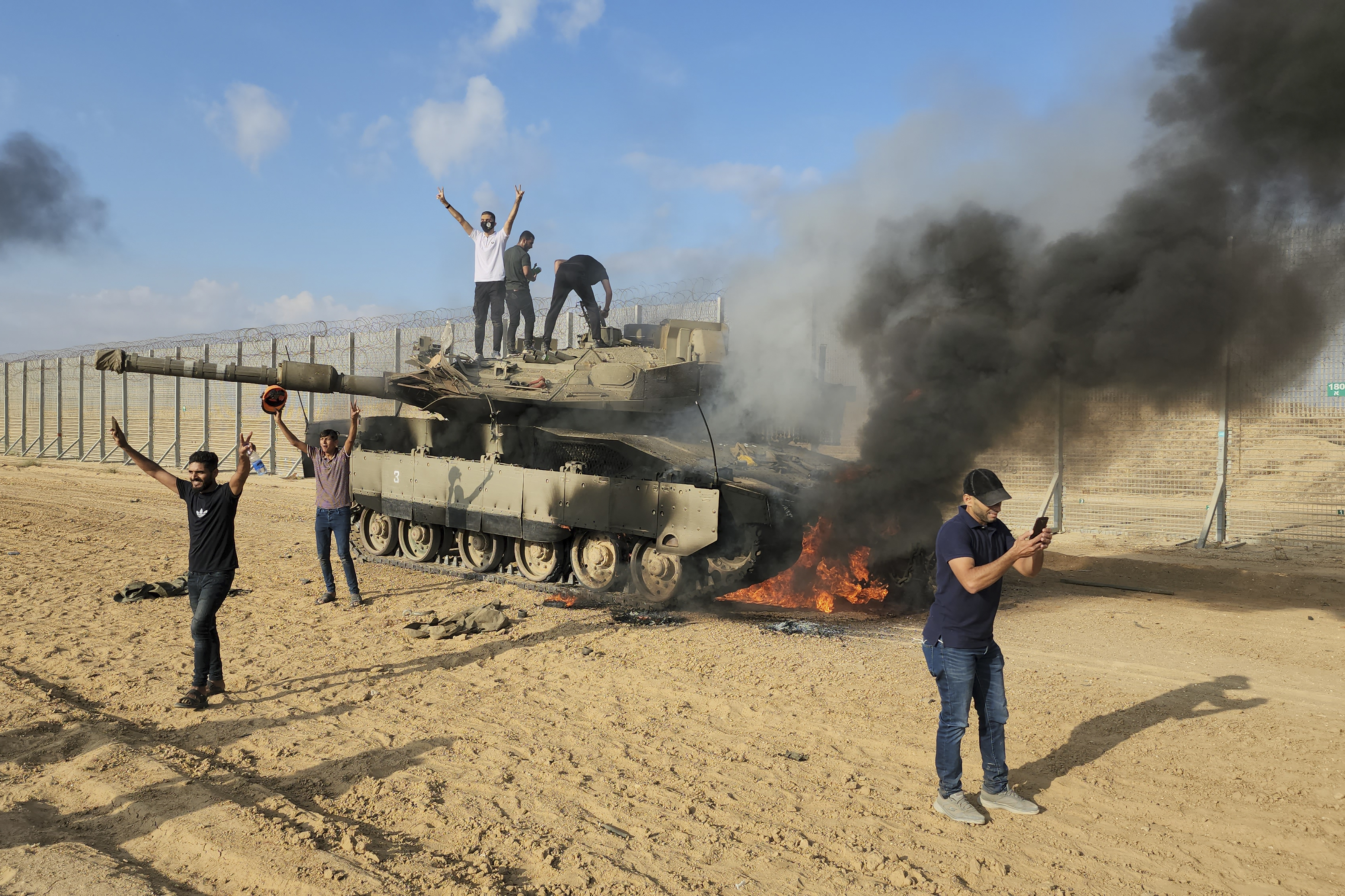Palestinians celebrate by a destroyed Israeli tank at the Gaza Strip fence east of Khan Younis, October 7, 2023