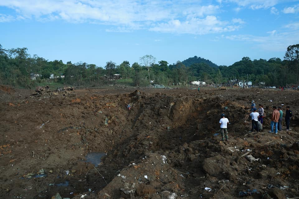 A massive crater left by the attack. Some poeple are standing inside it