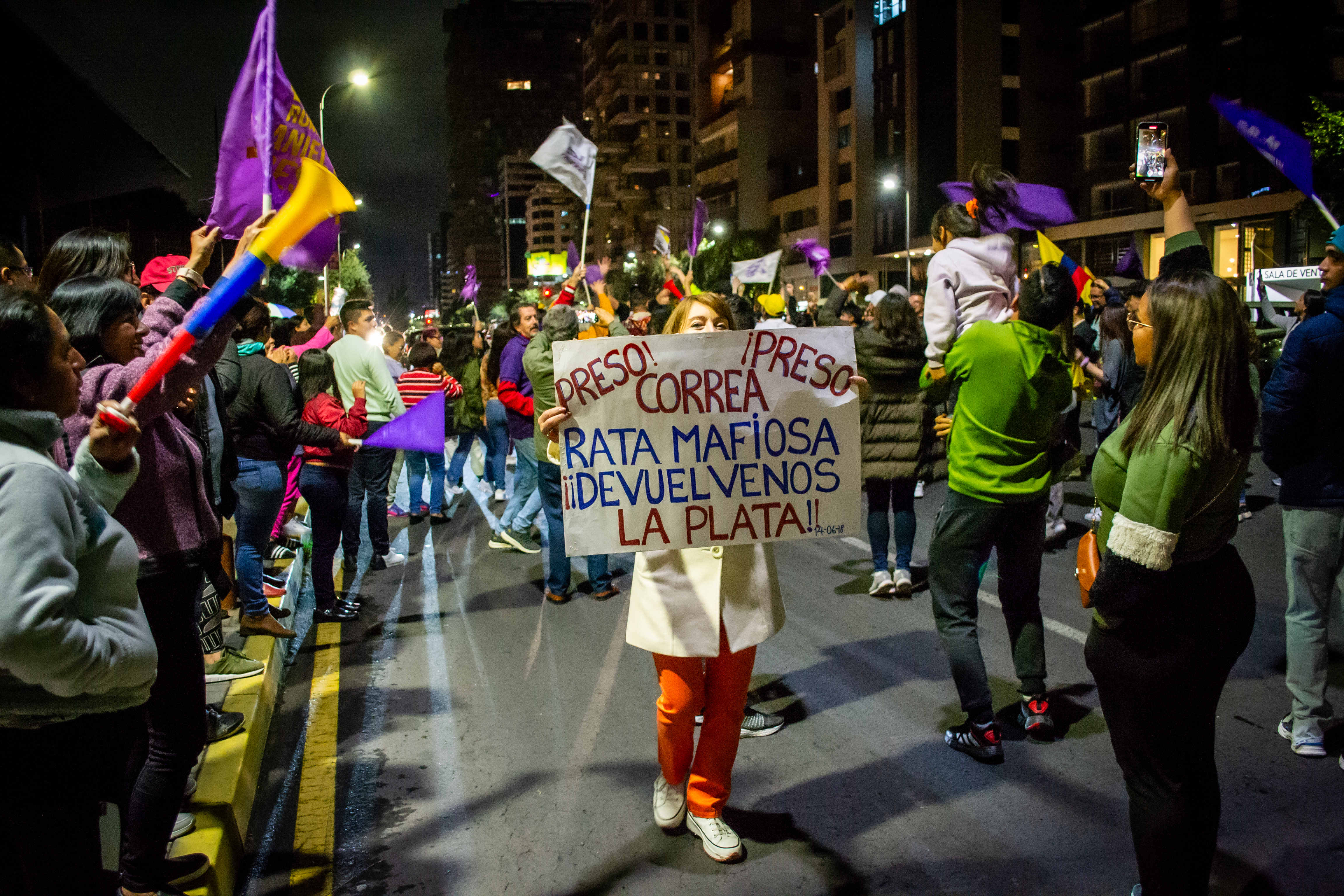 A woman holds up a hand-painted sign, as revellers gather on either side of the street.