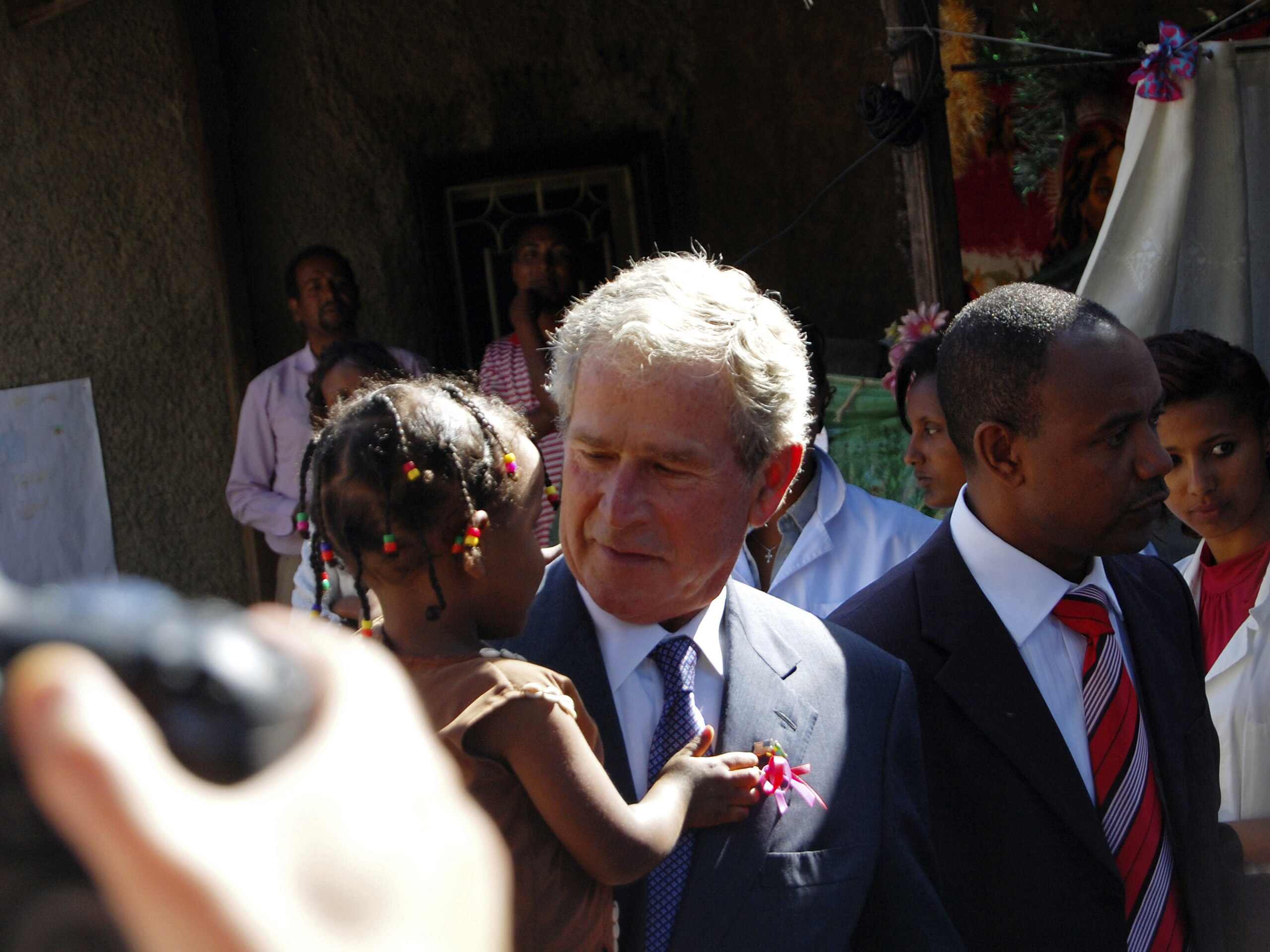 George W Bush, wearing a suit and tie, holds a little girl in his arms as he visits Ethiopia.