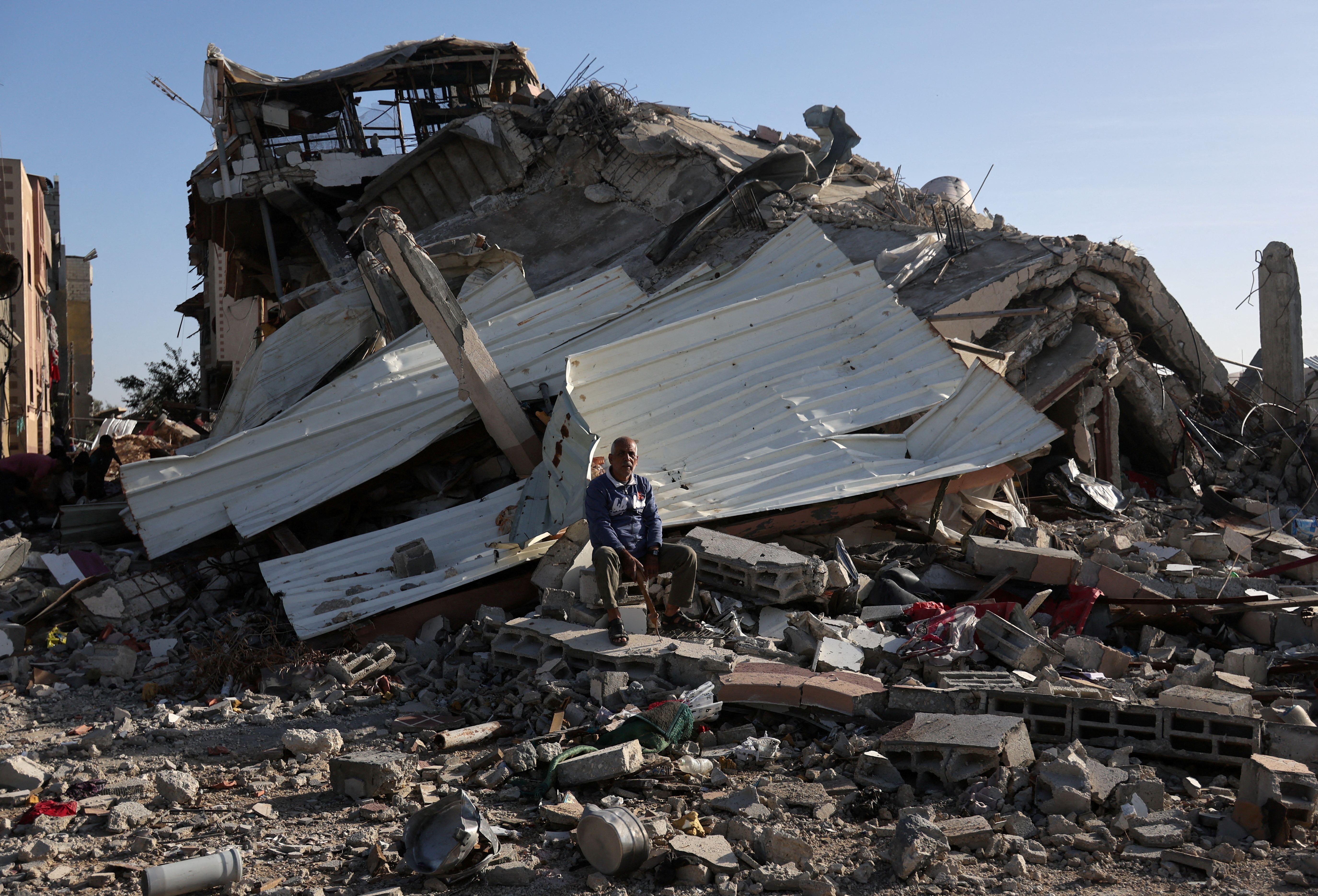 A Palestinian man sits on the rubble of a destroyed house