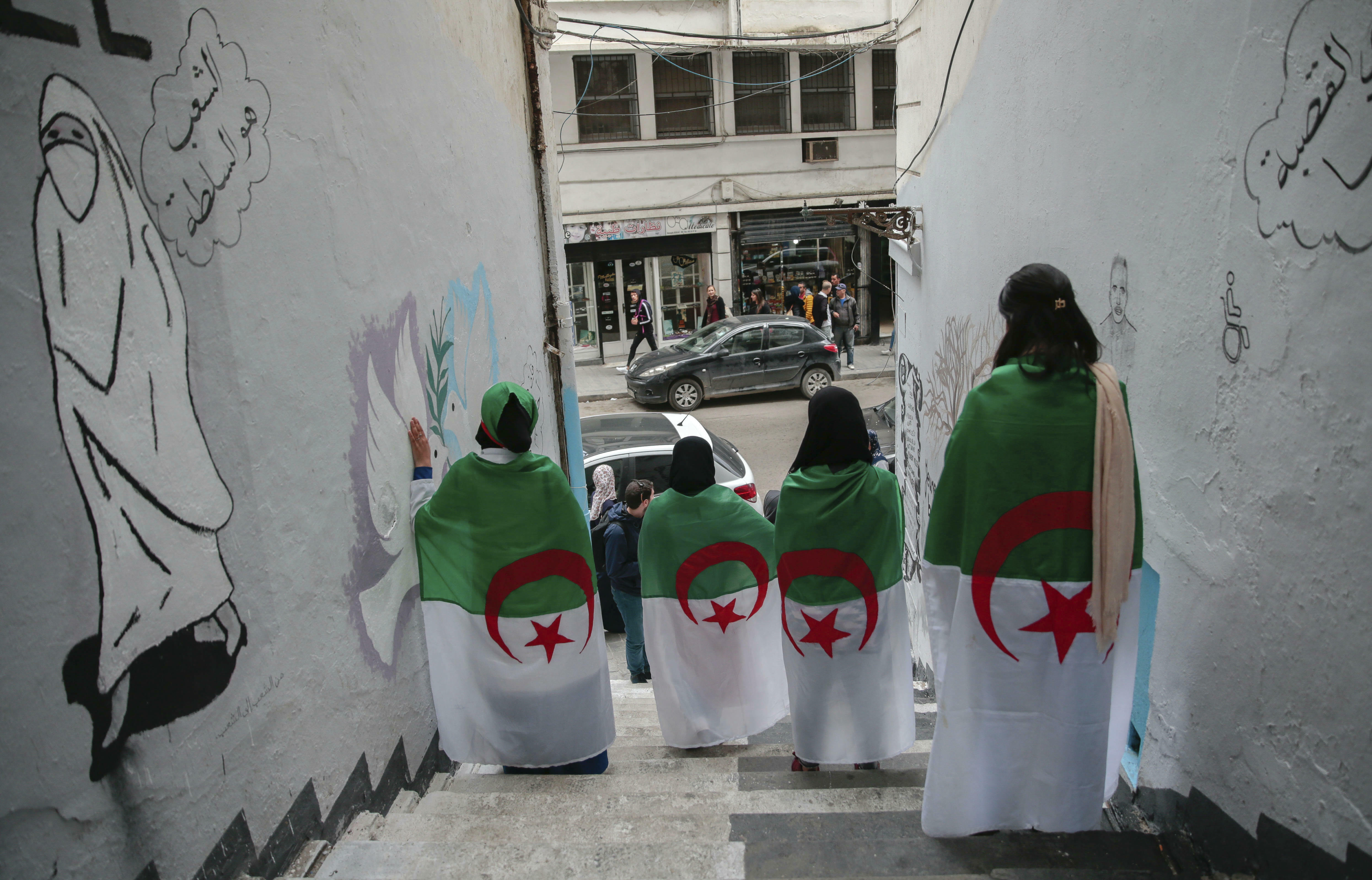 Young Algerian women pose next to street art supporting the protest movement in Algiers, Algeria. The writing in Arabic reads ‘The people are the authority’, on April 10, 2019