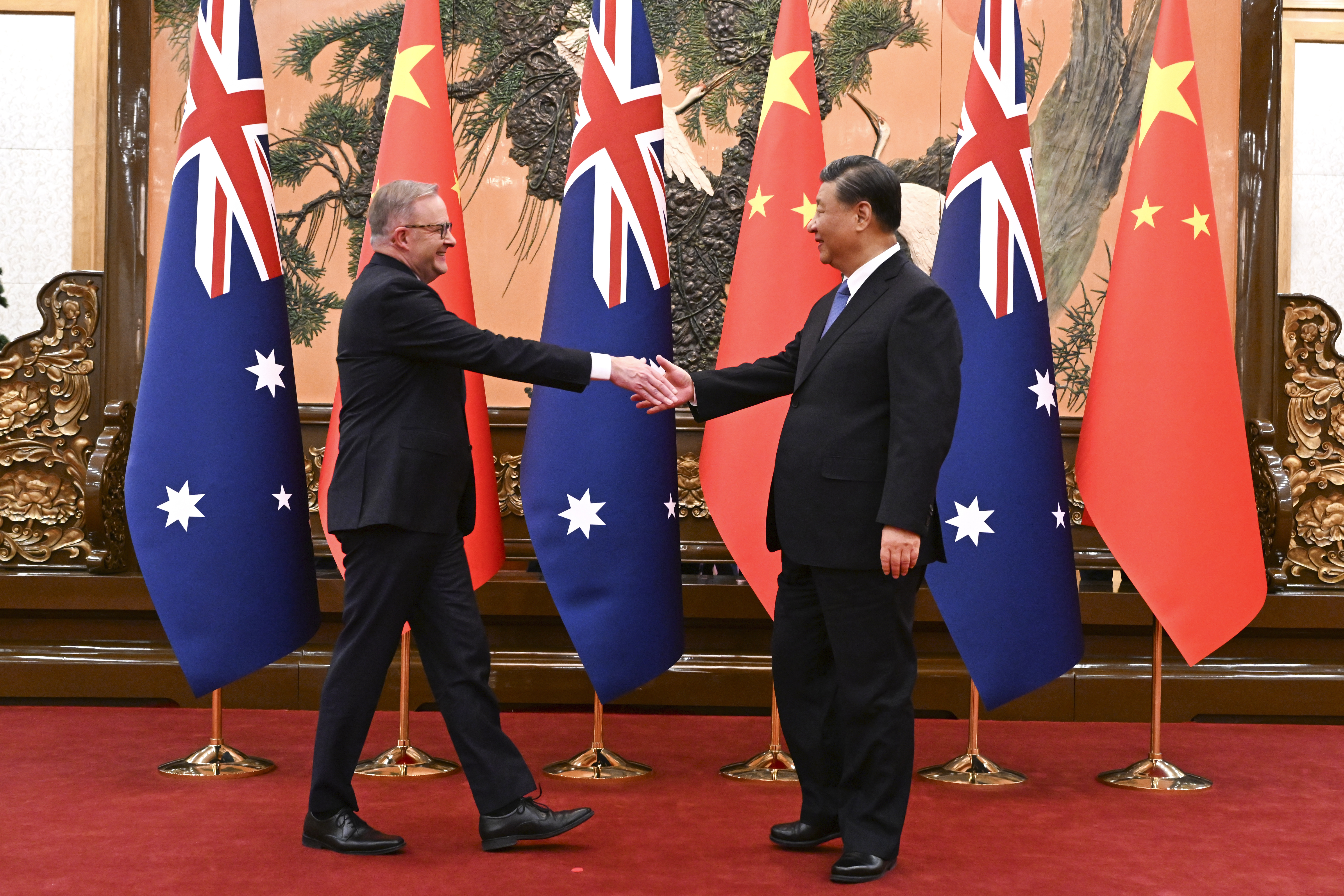 Anthony Albanese and Xi Jinping walking towards each other and shaking hands. They are smiling. The flags of Australia and China are behind them