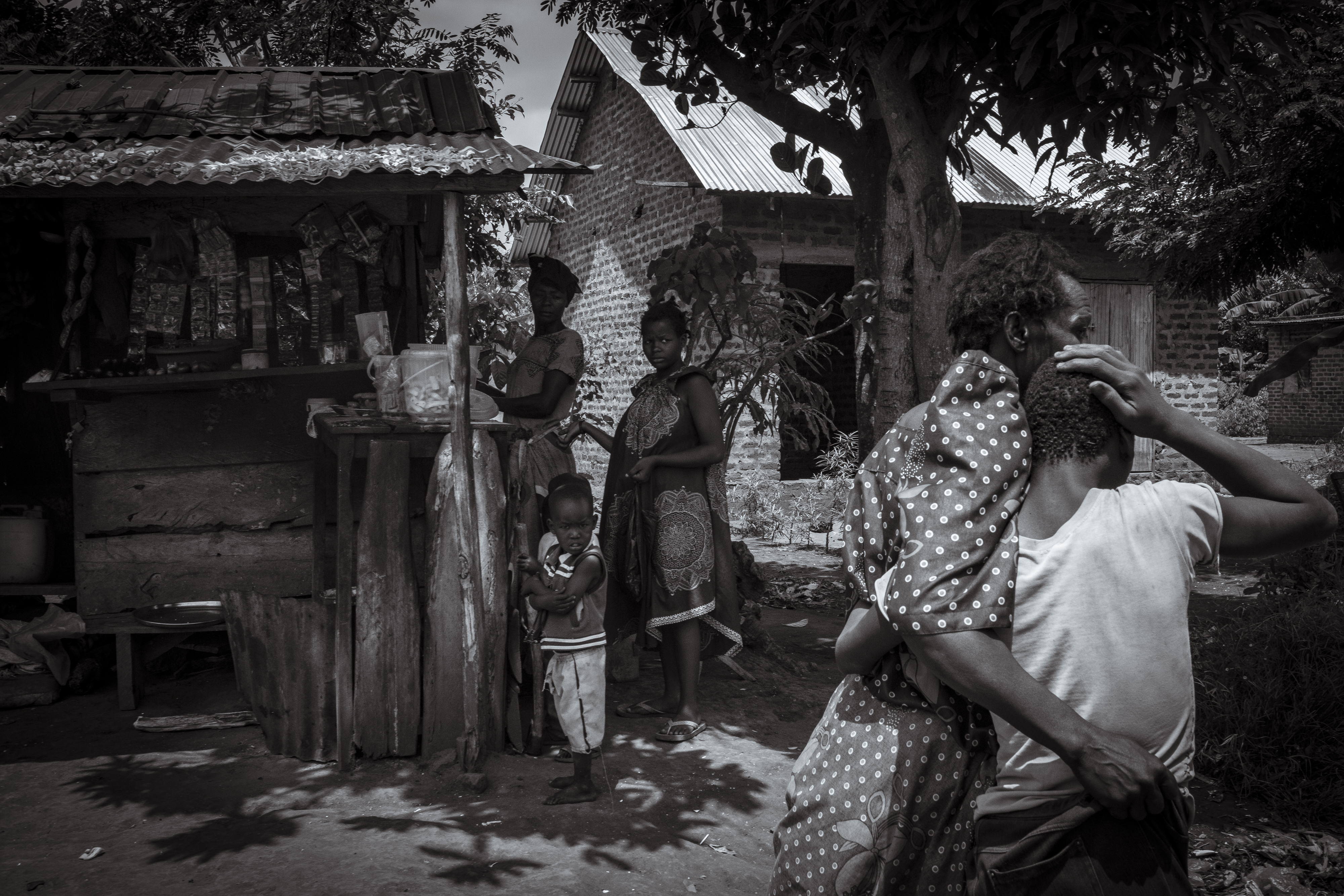 Lovinsa Namwebya comforts her son, Perez Mbwase, who lives with severe autism, as they are watched by local shopkeepers and children on a walk to Namwebya's farming field