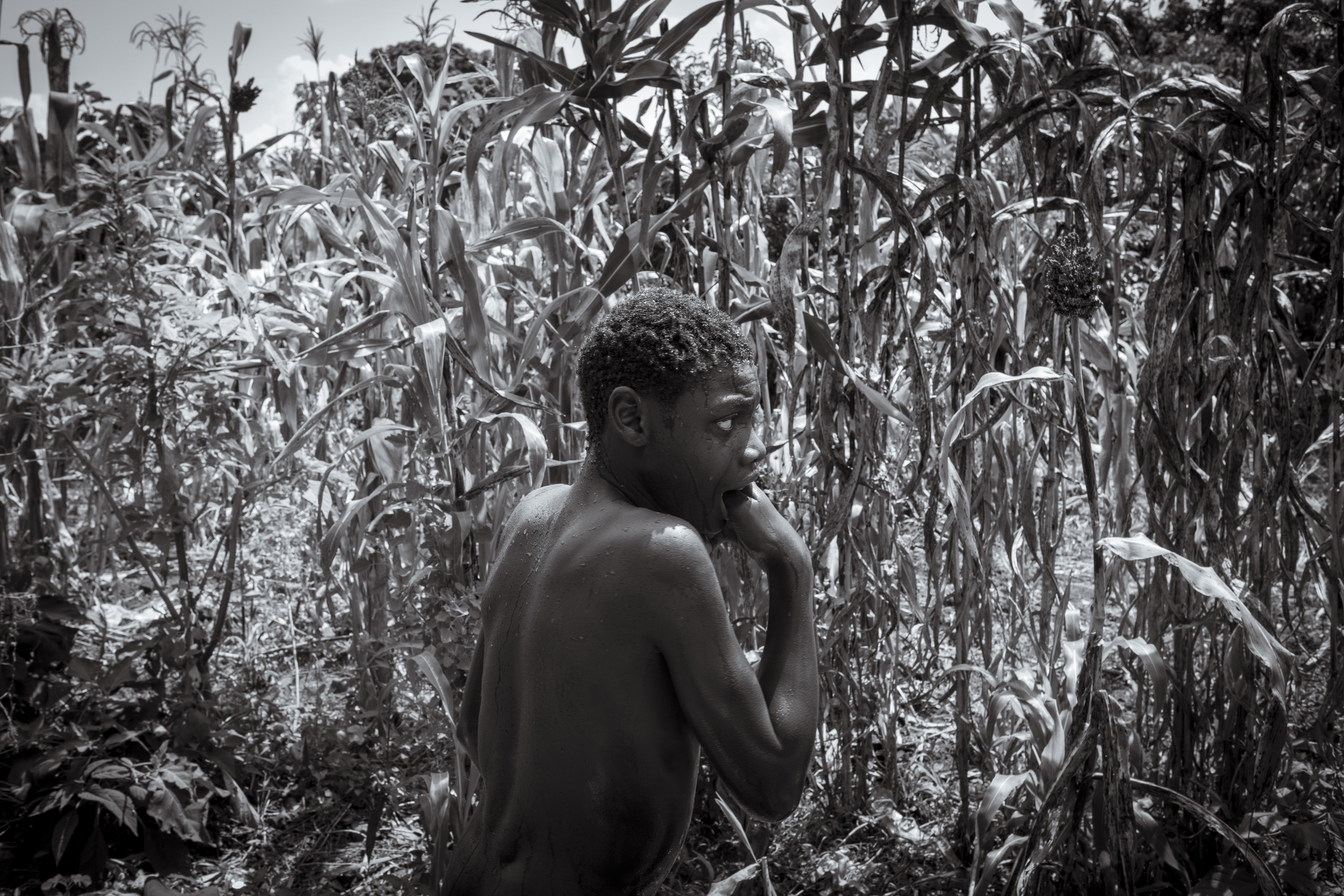 Perez Mwase cowers in the family maize field after being bathed by his mother Lovinsa Namwebya. Perez, 19, lives with severe autism