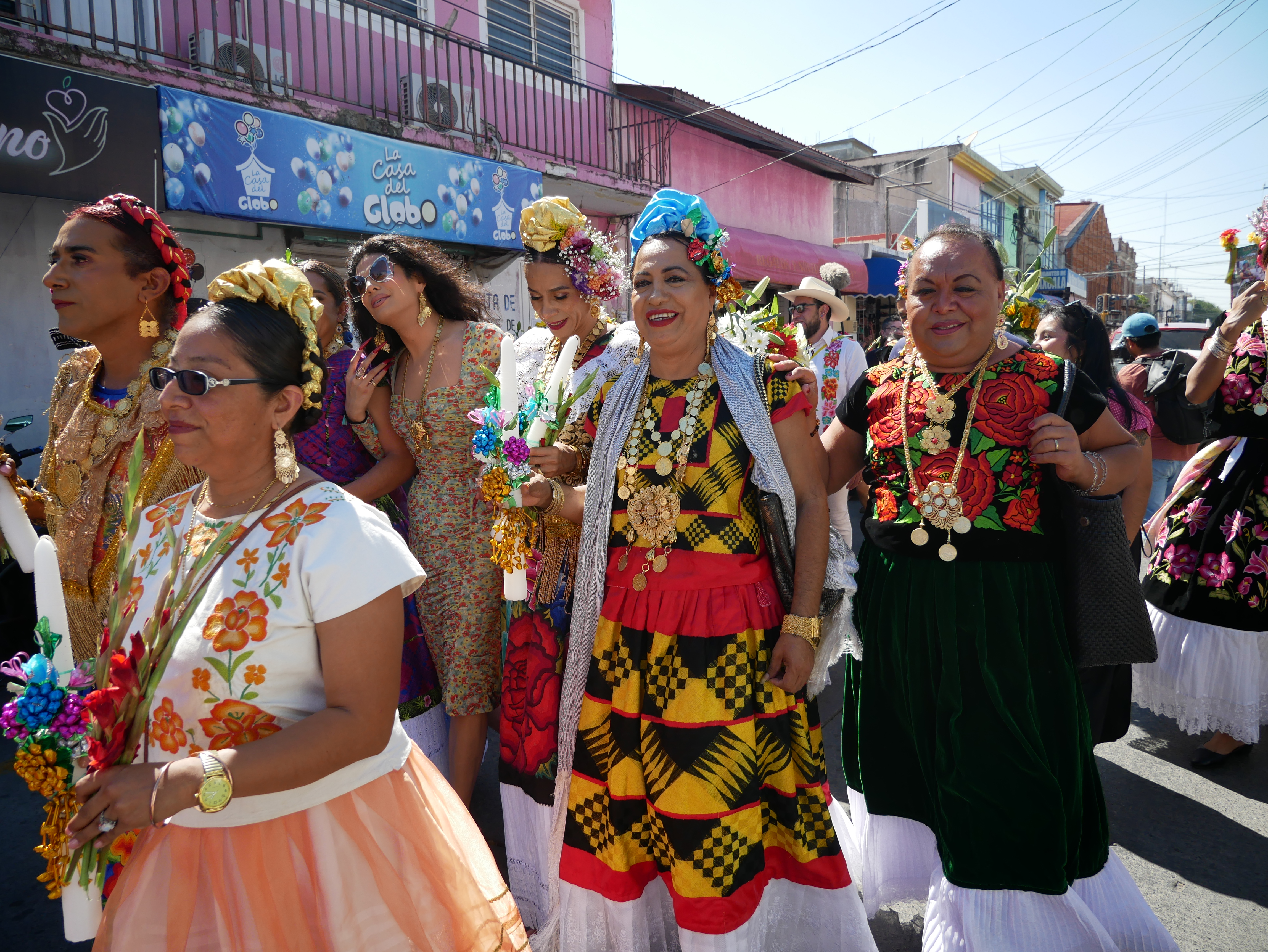 Muxes — members of an Indigenous third gender community — parade through the streets in bright traditional dresses as they carry candles decorated with fabric flowers.