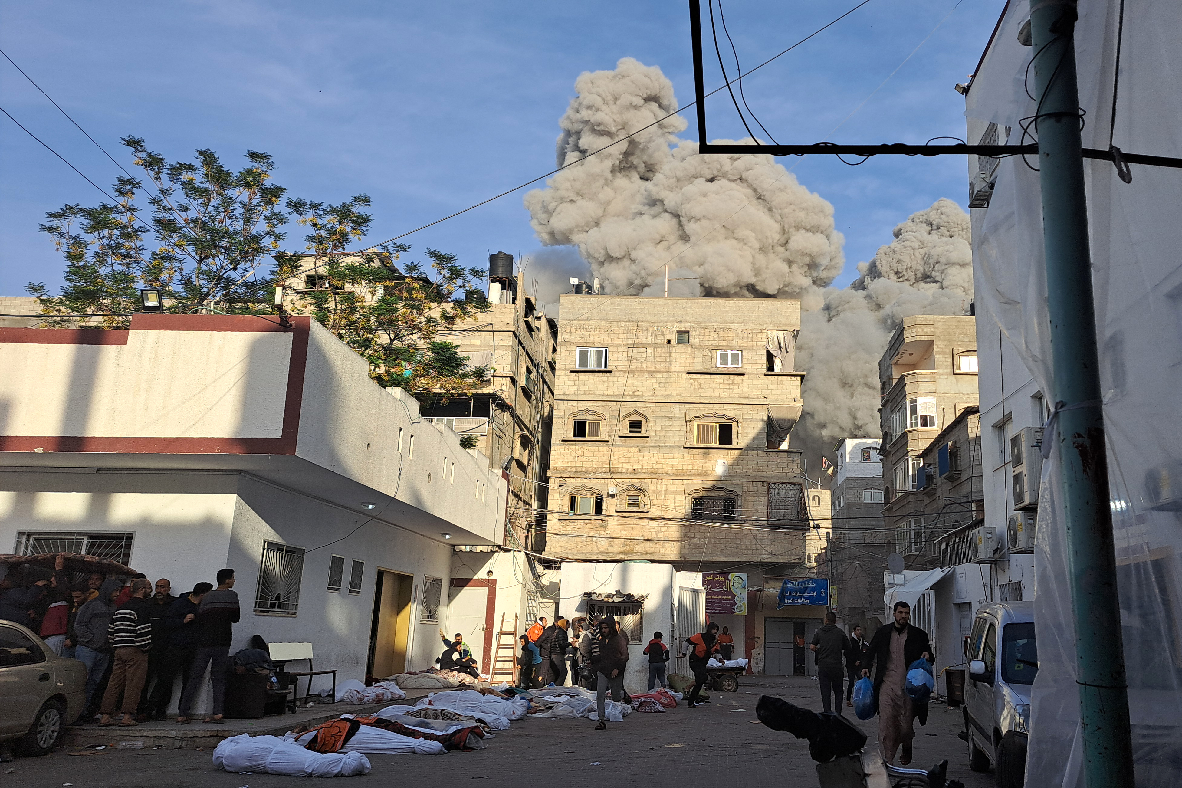 Palestinians running for shelter next to covered bodies after an Israeli air raid near the Kamal Adwan Hospital in Beit Lahia in the northern Gaza Strip