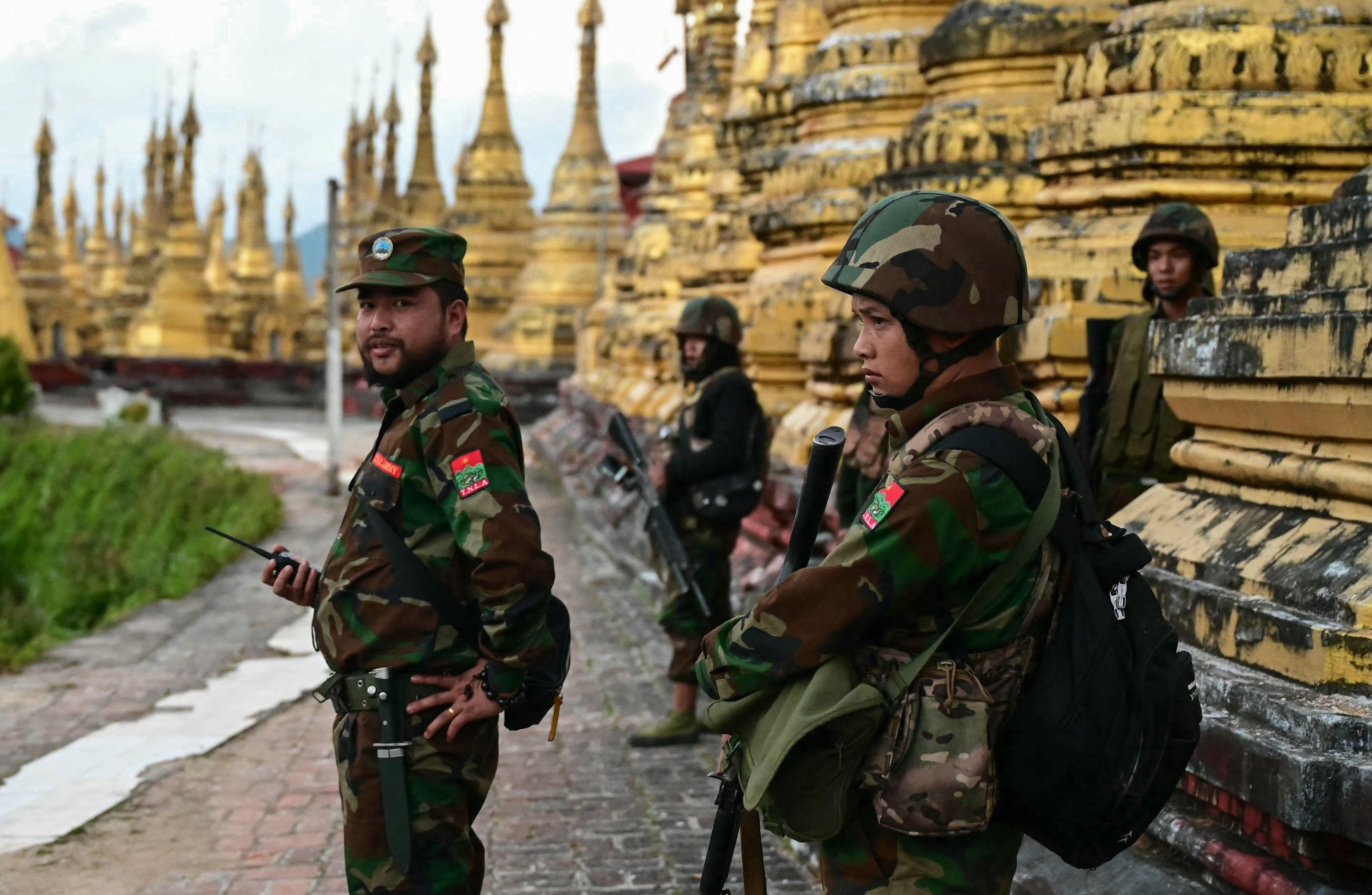 Ta'ang National Liberation Army (TNLA) standing guard in a temple area of a hill camp seized from Myanmar's military in Namhsan Township. The temple has golden stupas.