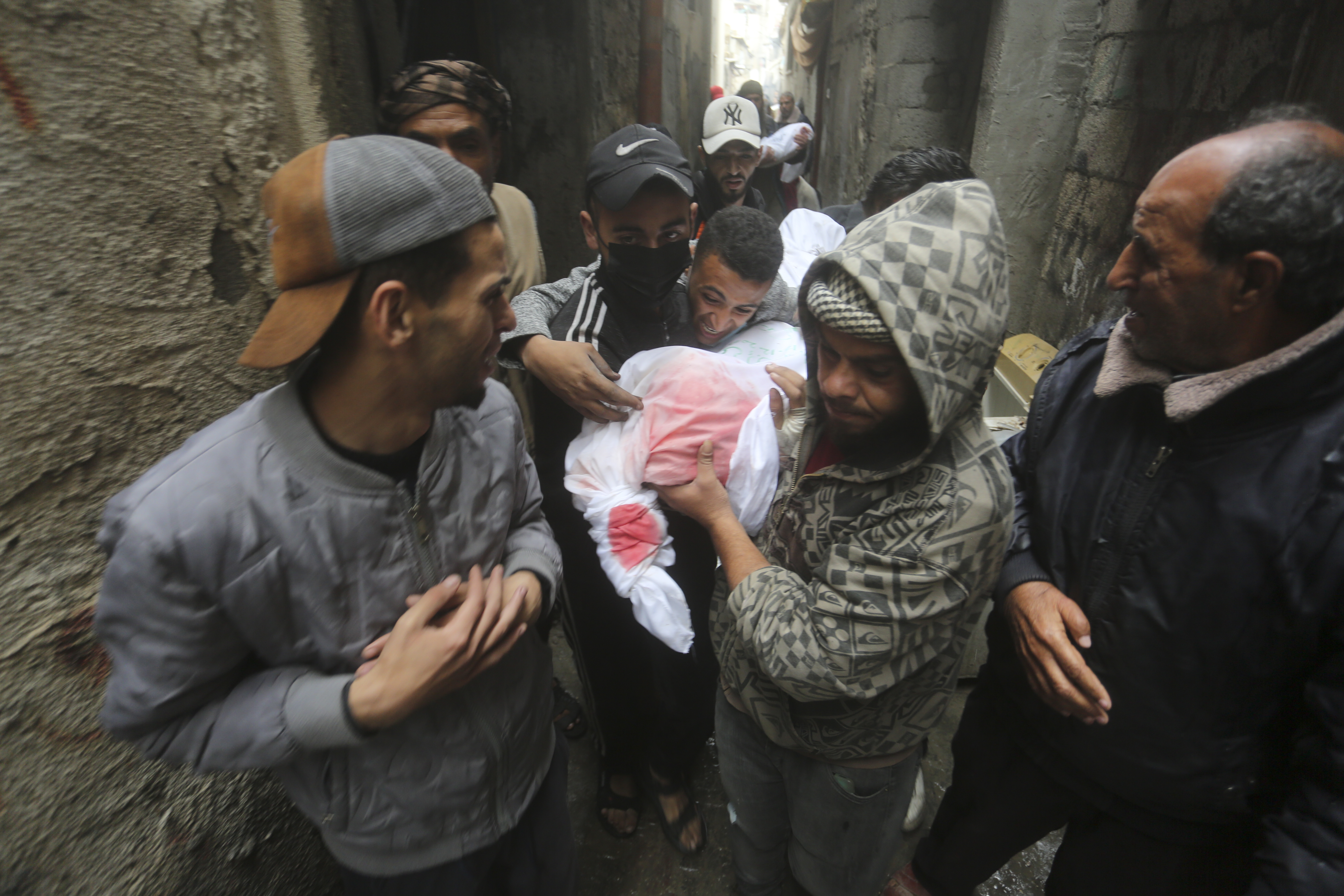 Palestinians carry a white bag with a body of someone killed in the Israeli bombardment through a narrow street