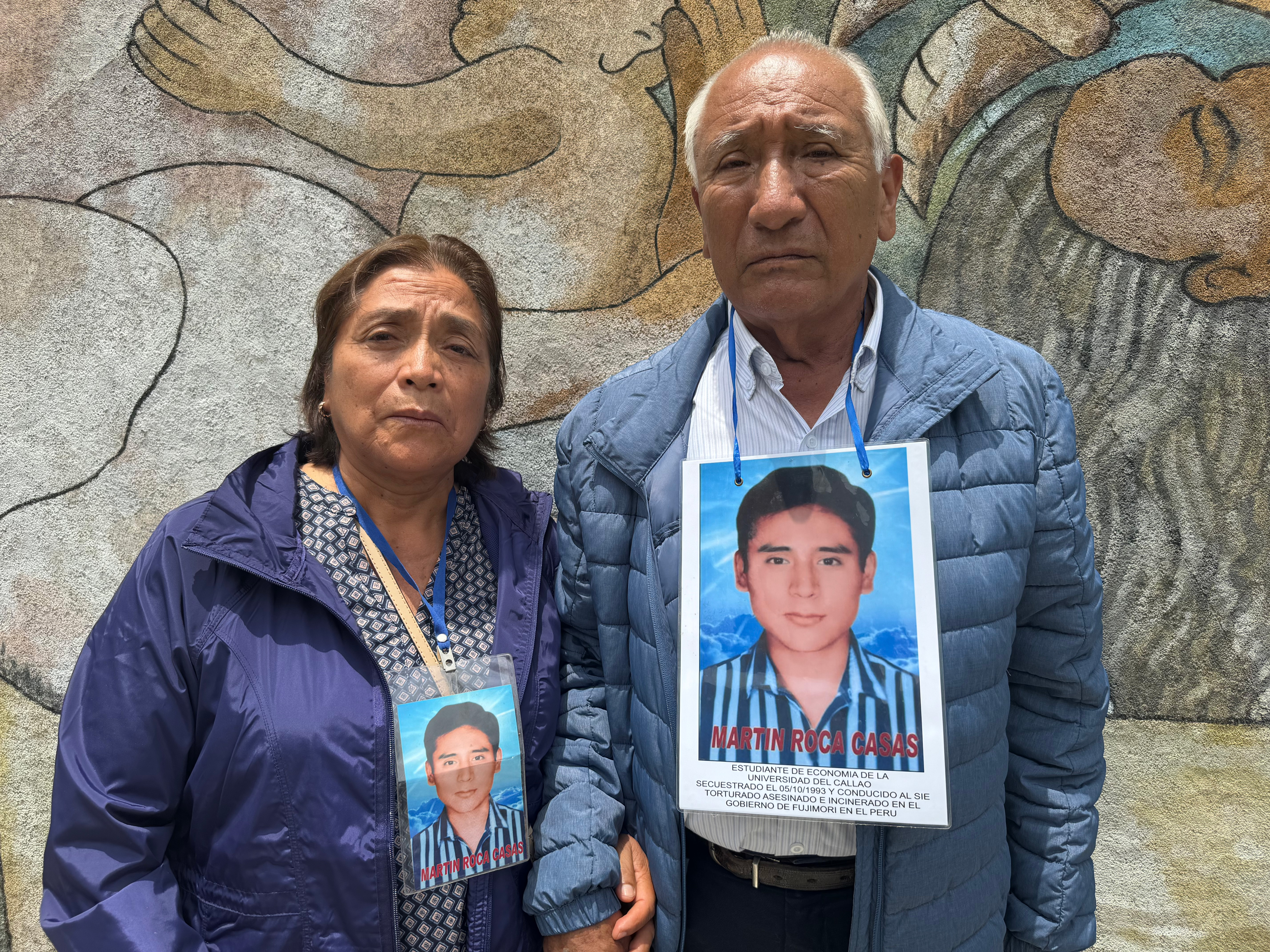 Javier Roca Obregón and his wife hold hands. Each of them wears a color photo around their neck featuring their missing son.