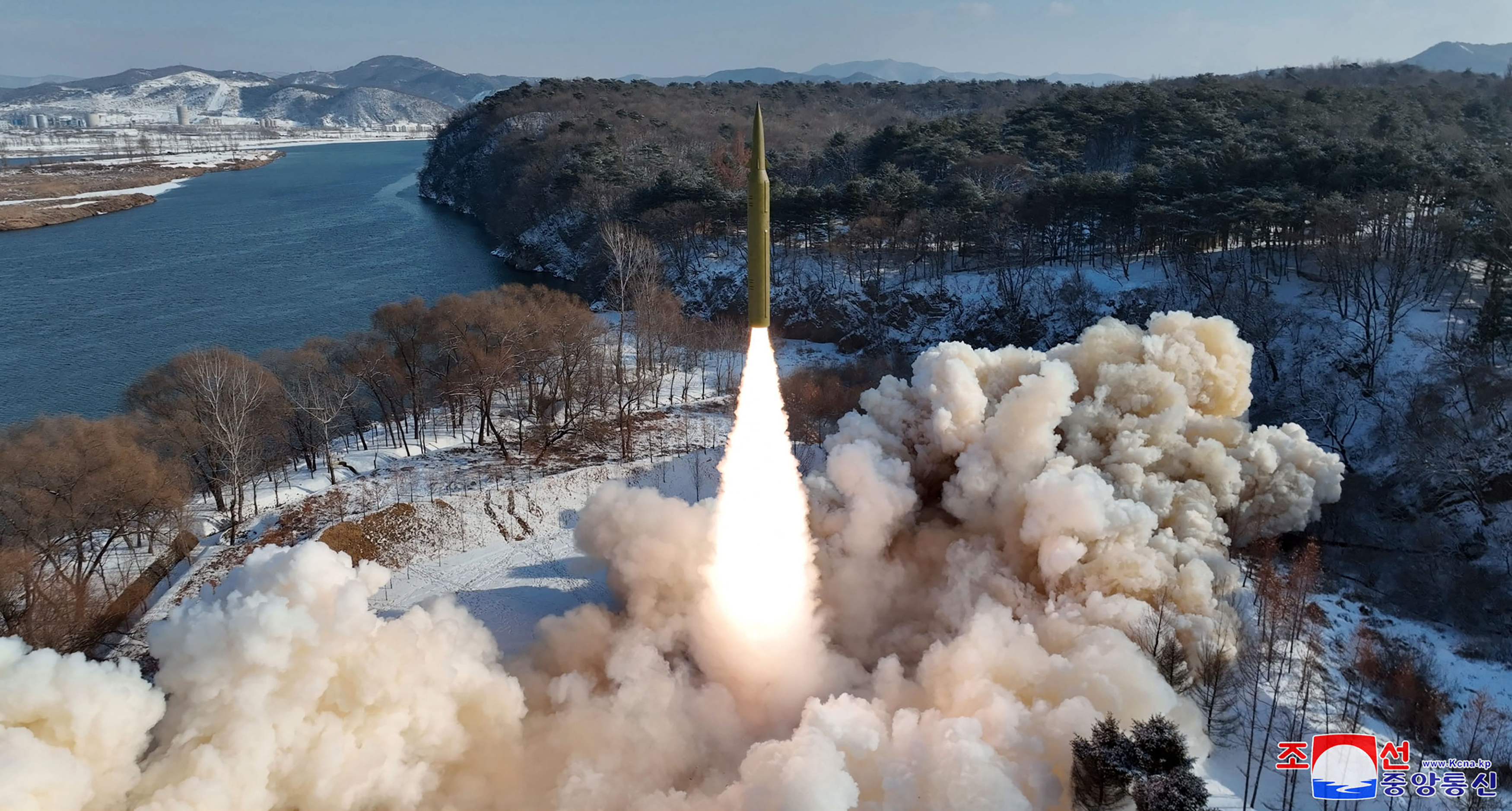 A missile being launched from land near the sea. There is lots of smoke and flame.