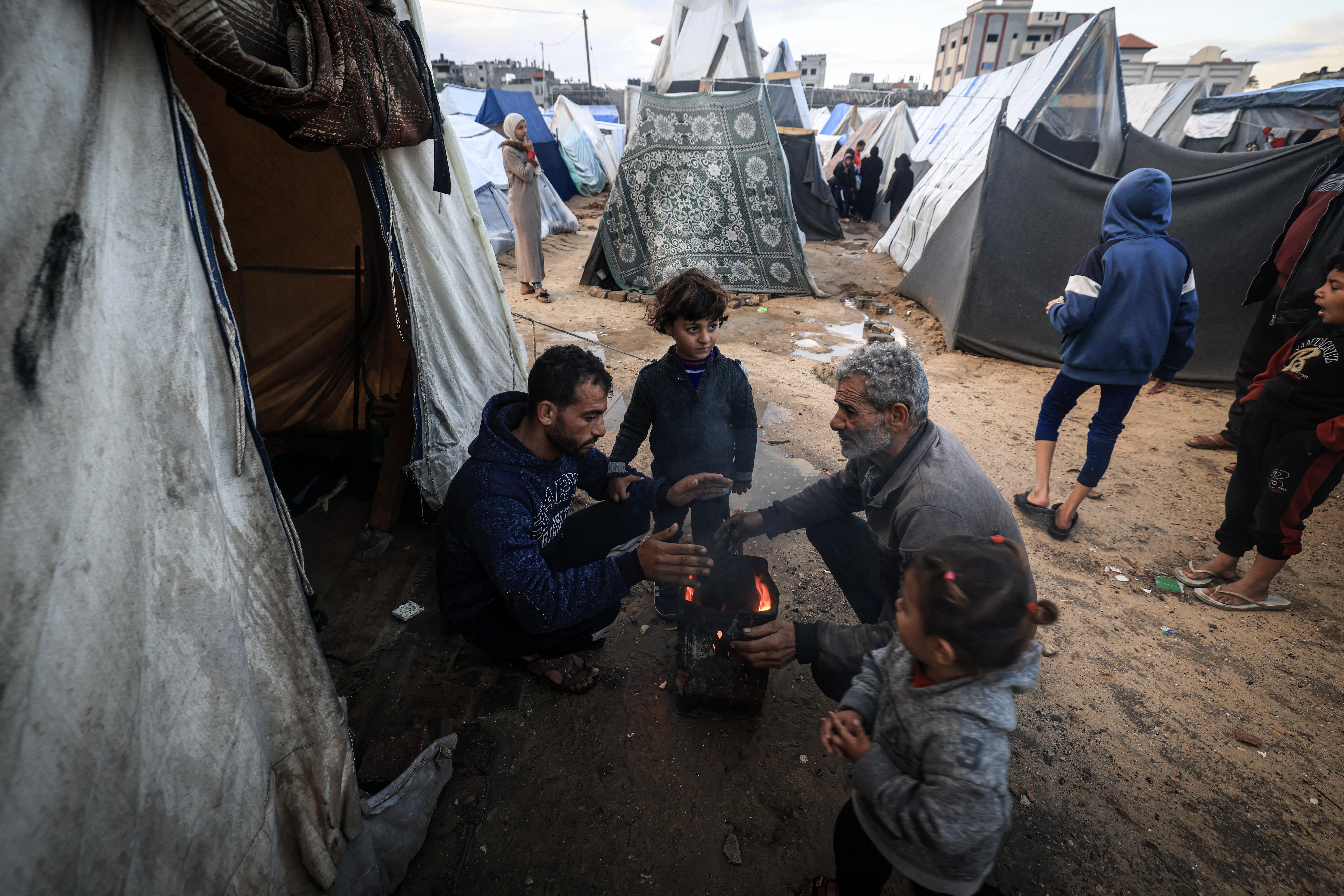 Displaced Palestinians try to warm up around a fire amid tents flooded by heavy rain