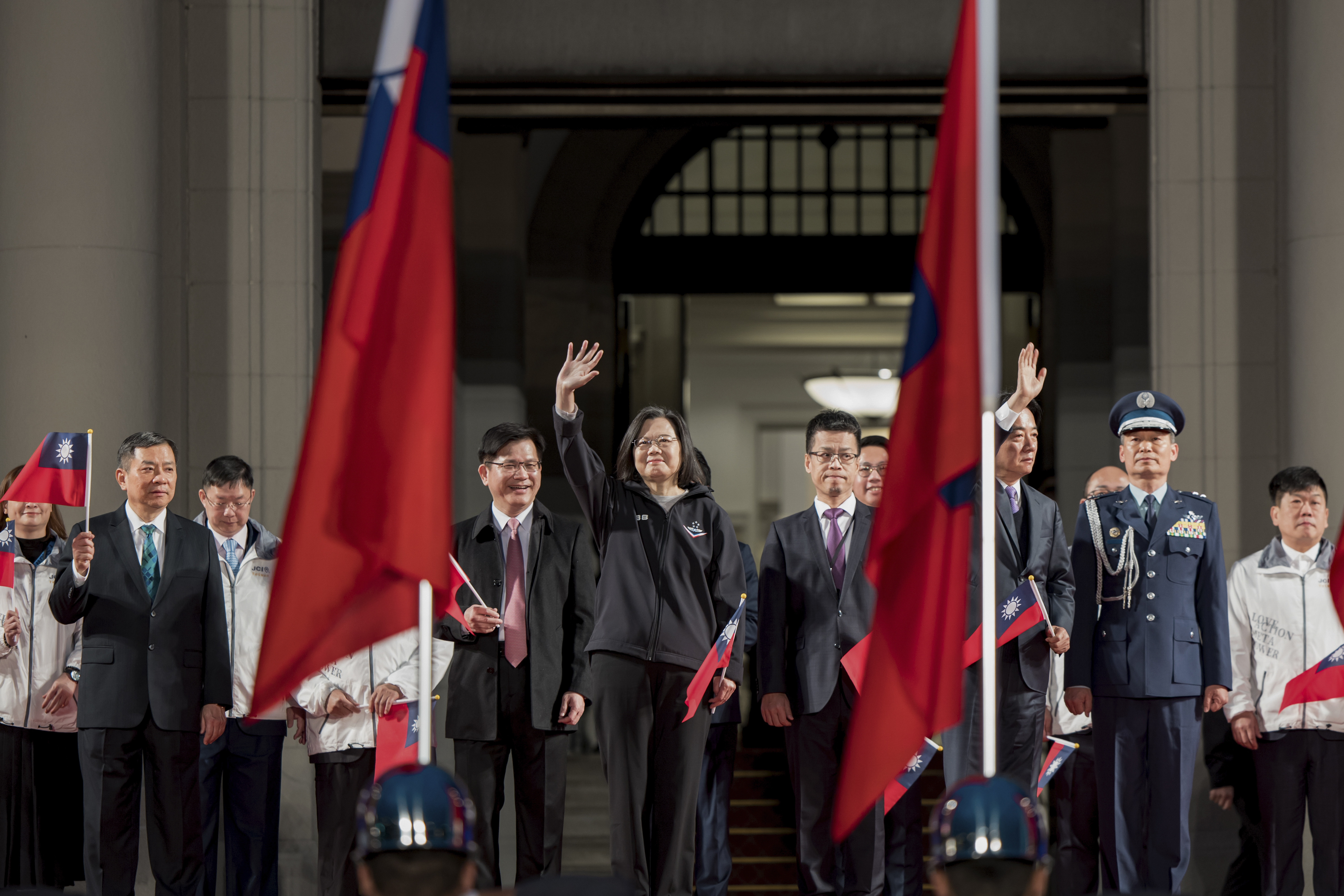 Tsai Ing-wen waving on the steps of the Presidential Office. She is standing between two Taiwan flags.
