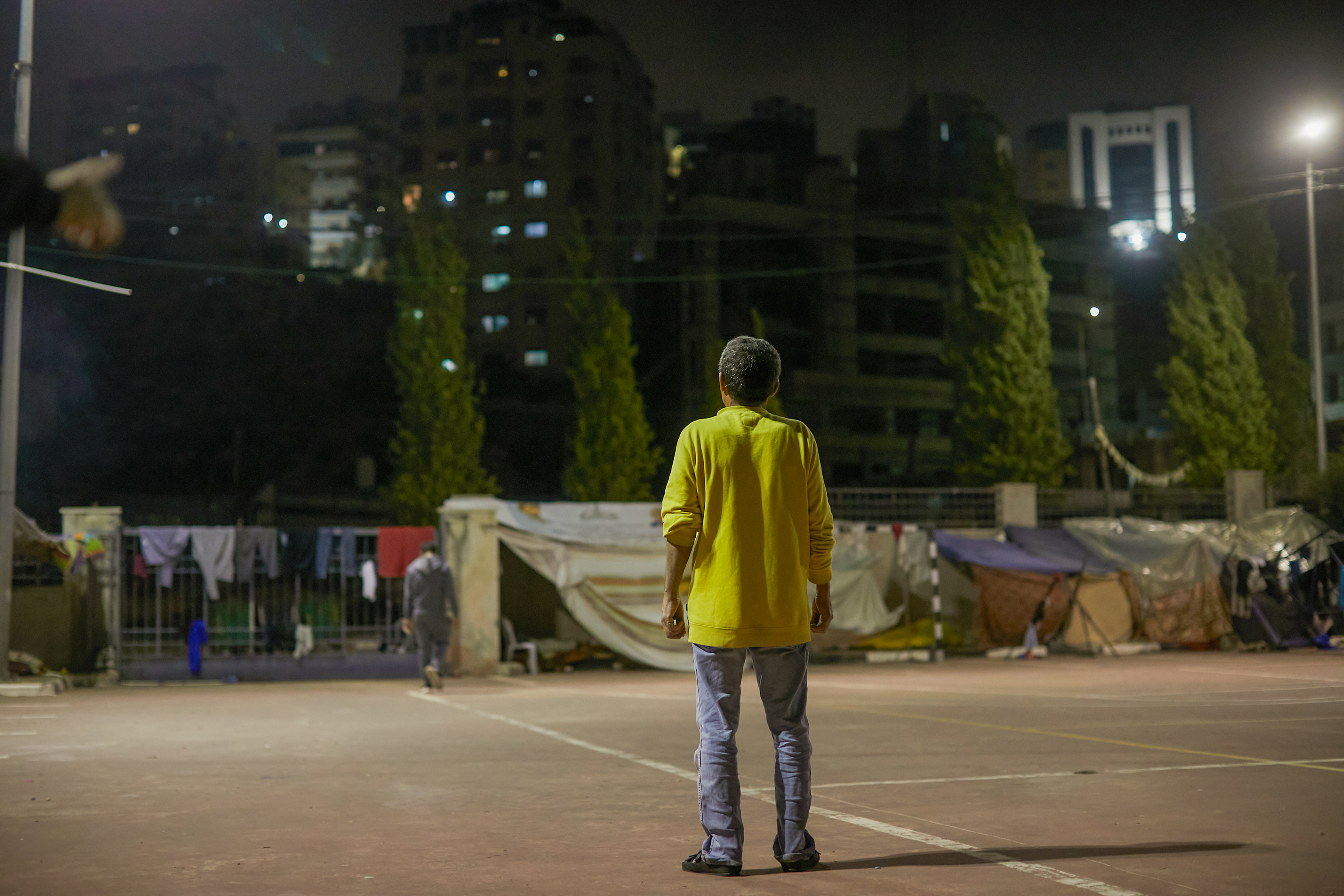 Nazir, in a yellow shirt, stands with his back to the camera