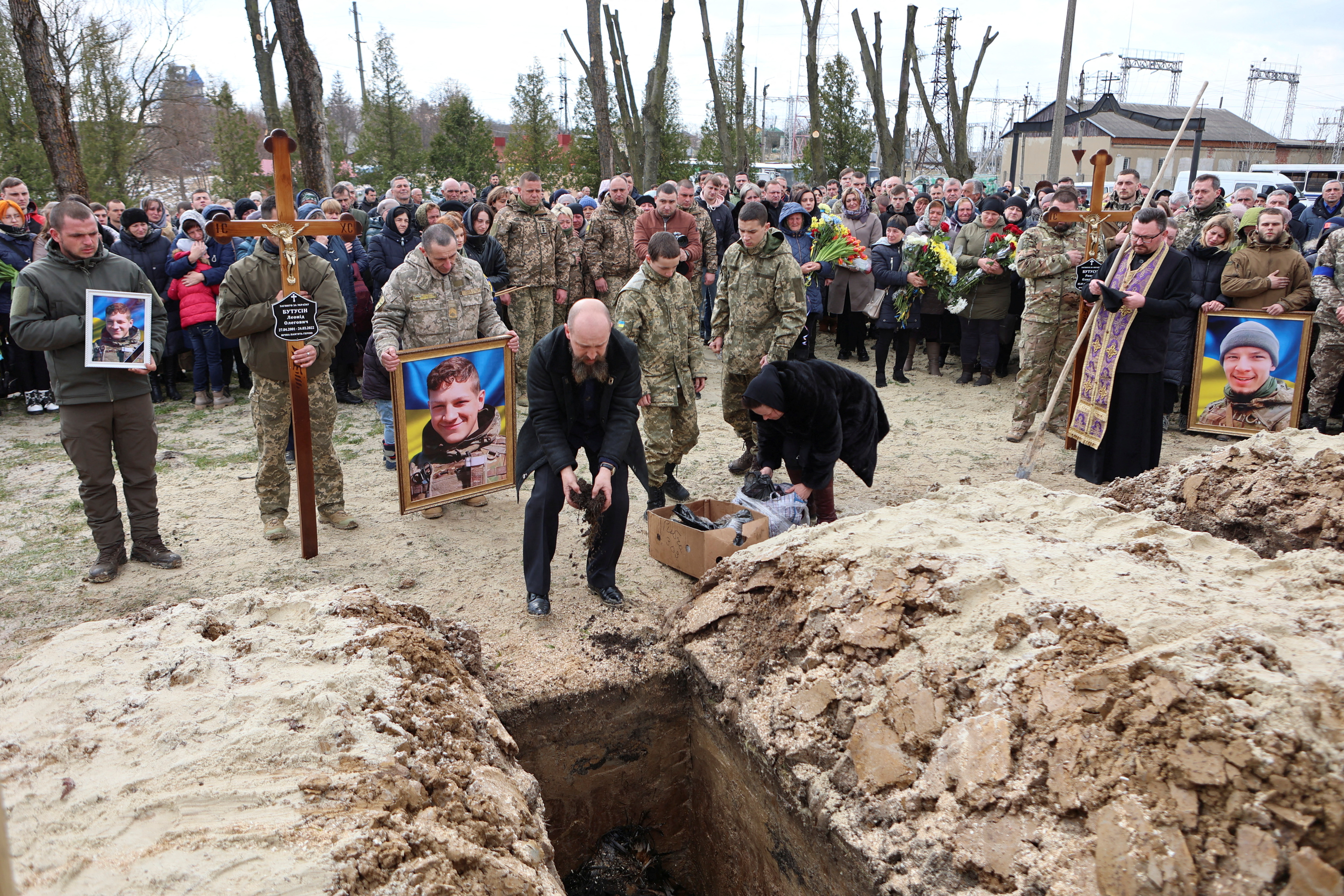 Oleg Butusin, father of brothers Roman and Leonid Butusin, amid Russia's invasion of Ukraine, pours earth into a grave during their funeral in Kalush, Ivano-Frankivsk region, Ukraine April 4, 2022