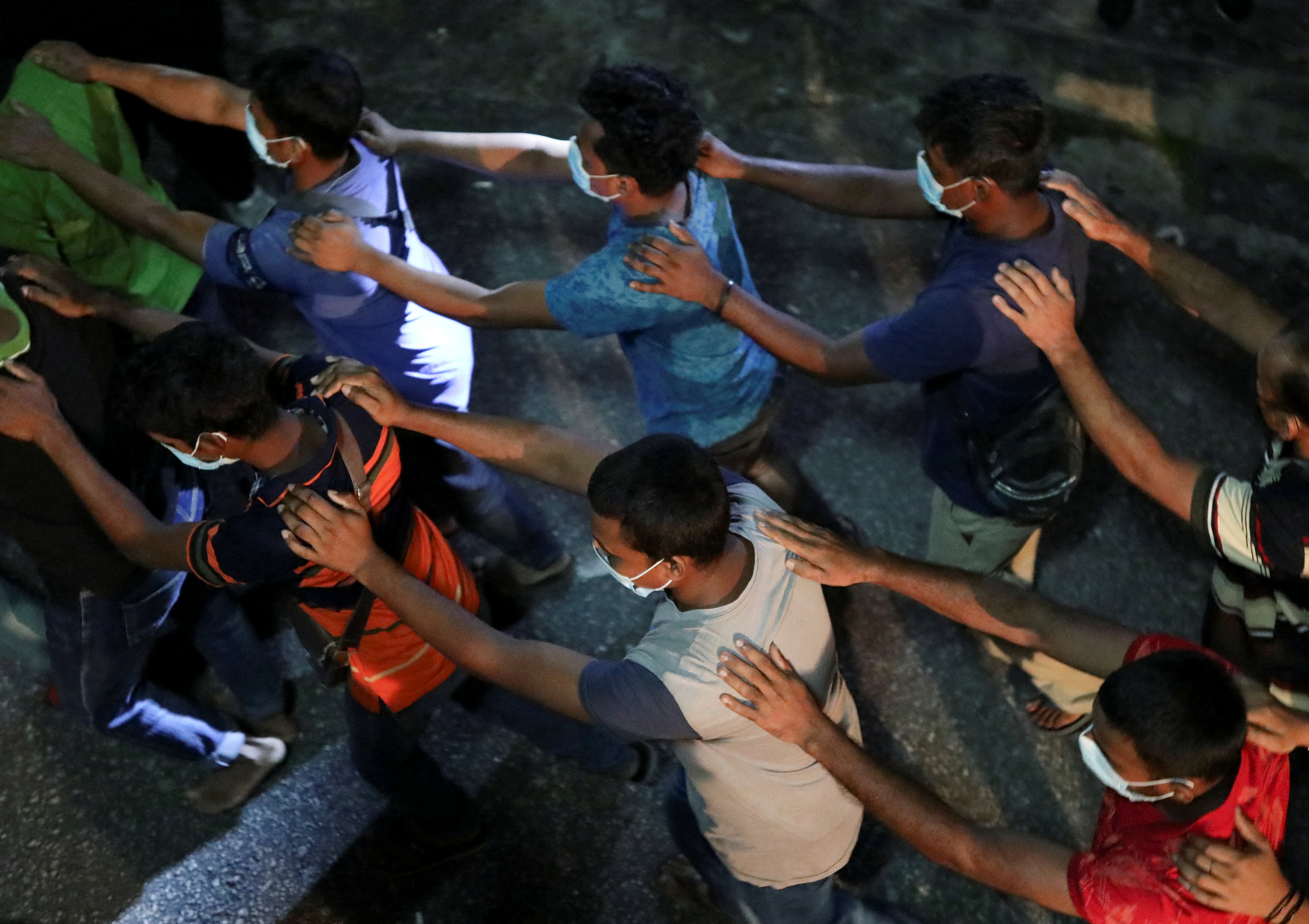 Undocumented migrants forced to walk away by police. They are walking in rows with their hands on the shoulders of the person in front.