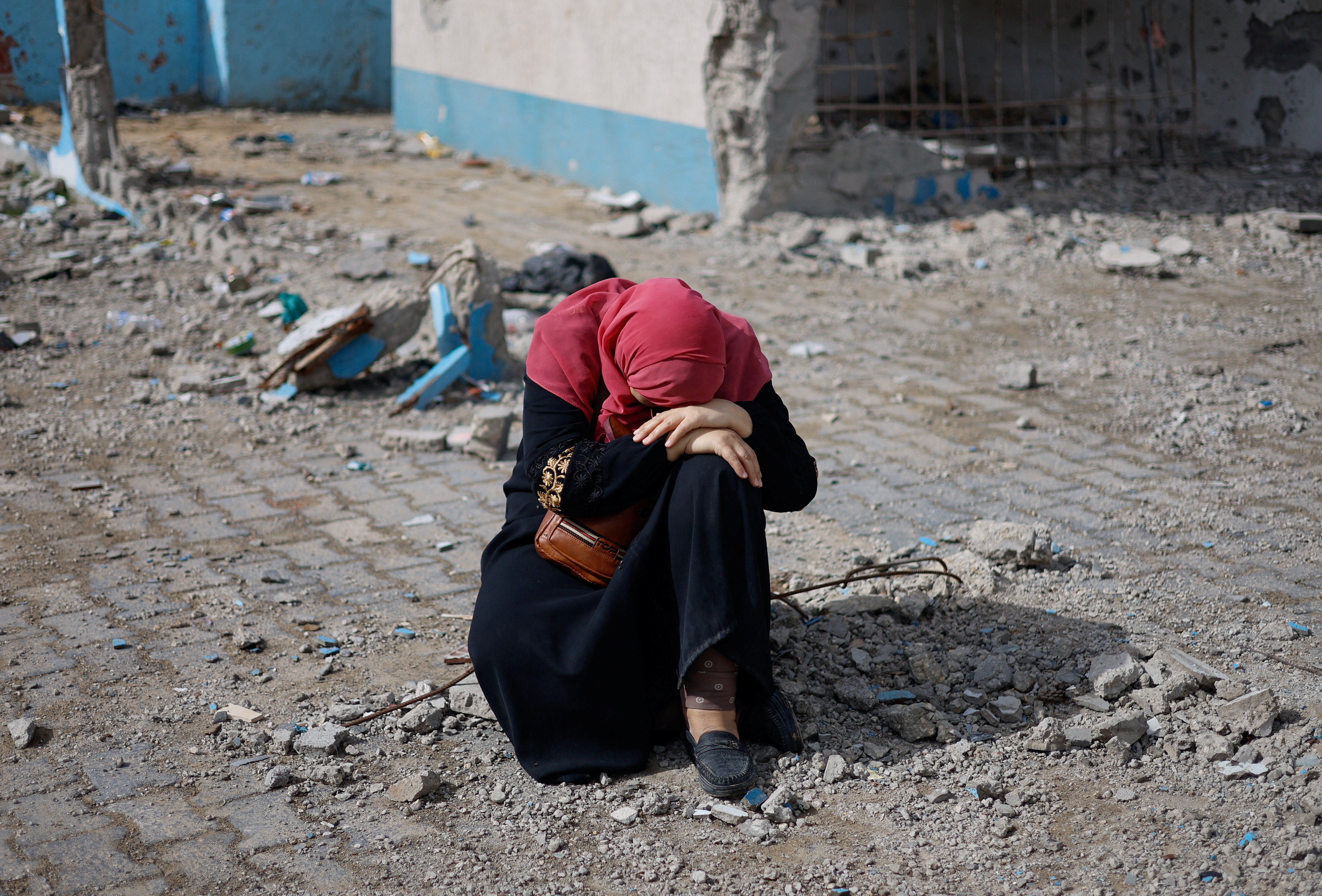 A woman rests next to a damaged building, as Palestinian arrive in Rafah after they were evacuated from Nasser hospital