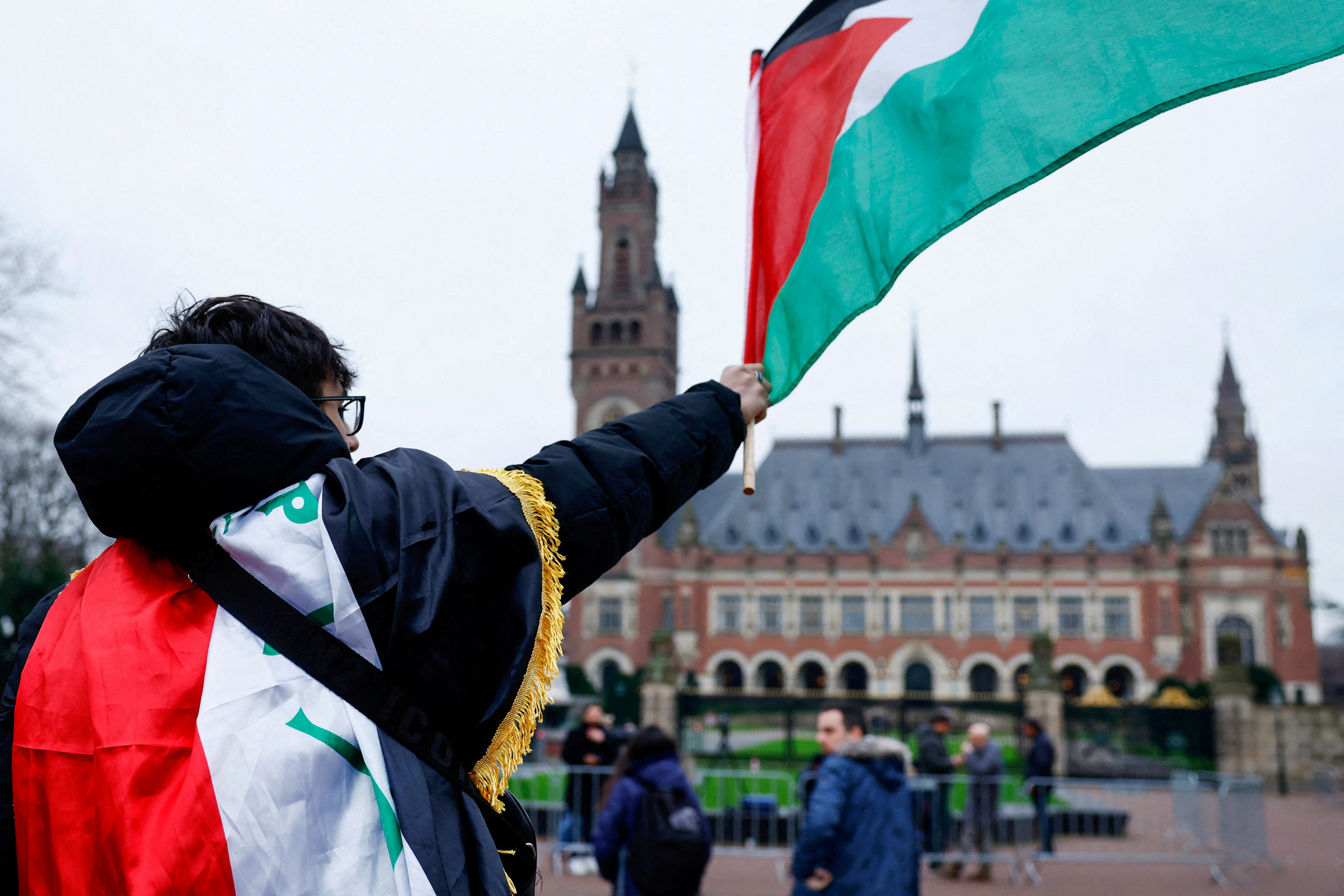 A man waves a Palestinian flag as people protest on the day of a public hearing held by The International Court of Justice (ICJ) to allow parties to give their views on the legal consequences of Israel's occupation of Palestinian territories before eventually issuing a non-binding legal opinion, in The Hague, Netherlands, February 21, 2024. [Piroschka van de Wouw/Reuters]