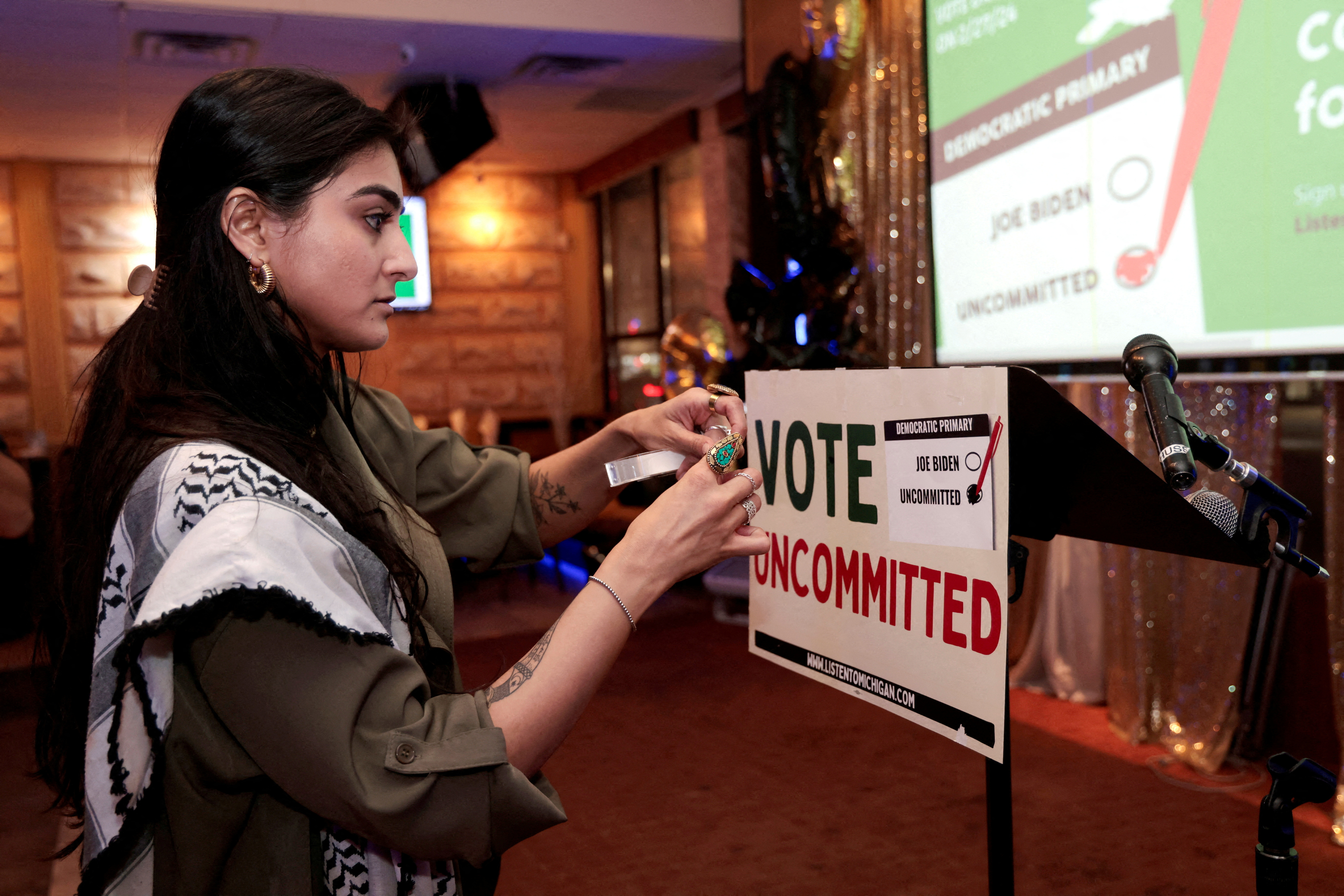 Activist Natalia Latif tapes a ‘Vote Uncommitted’ sign on the speaker’s podium during an election night gathering in Dearborn, Michigan