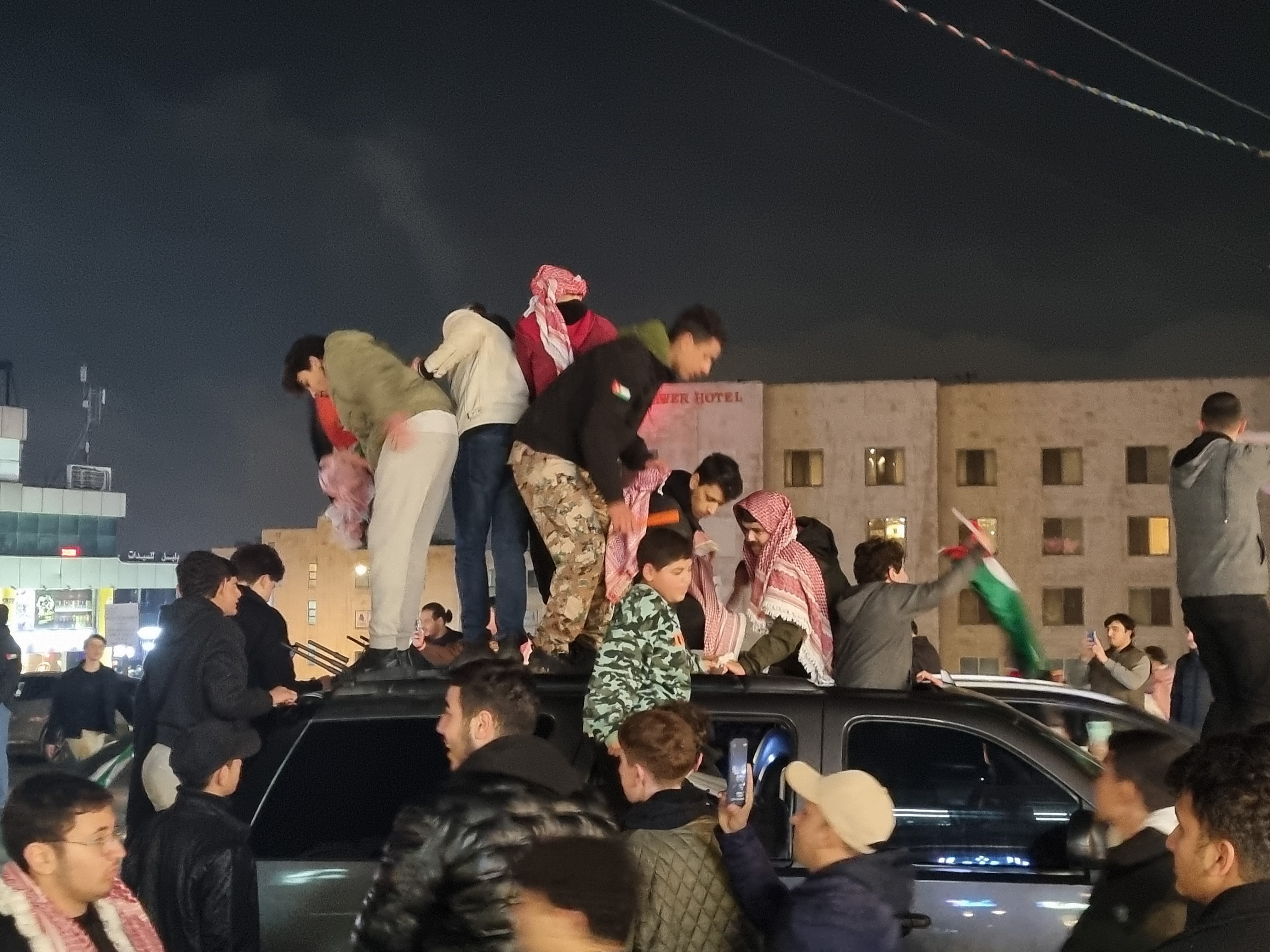 Jordanian fans climb on a car as they celebrate their semifinal win
