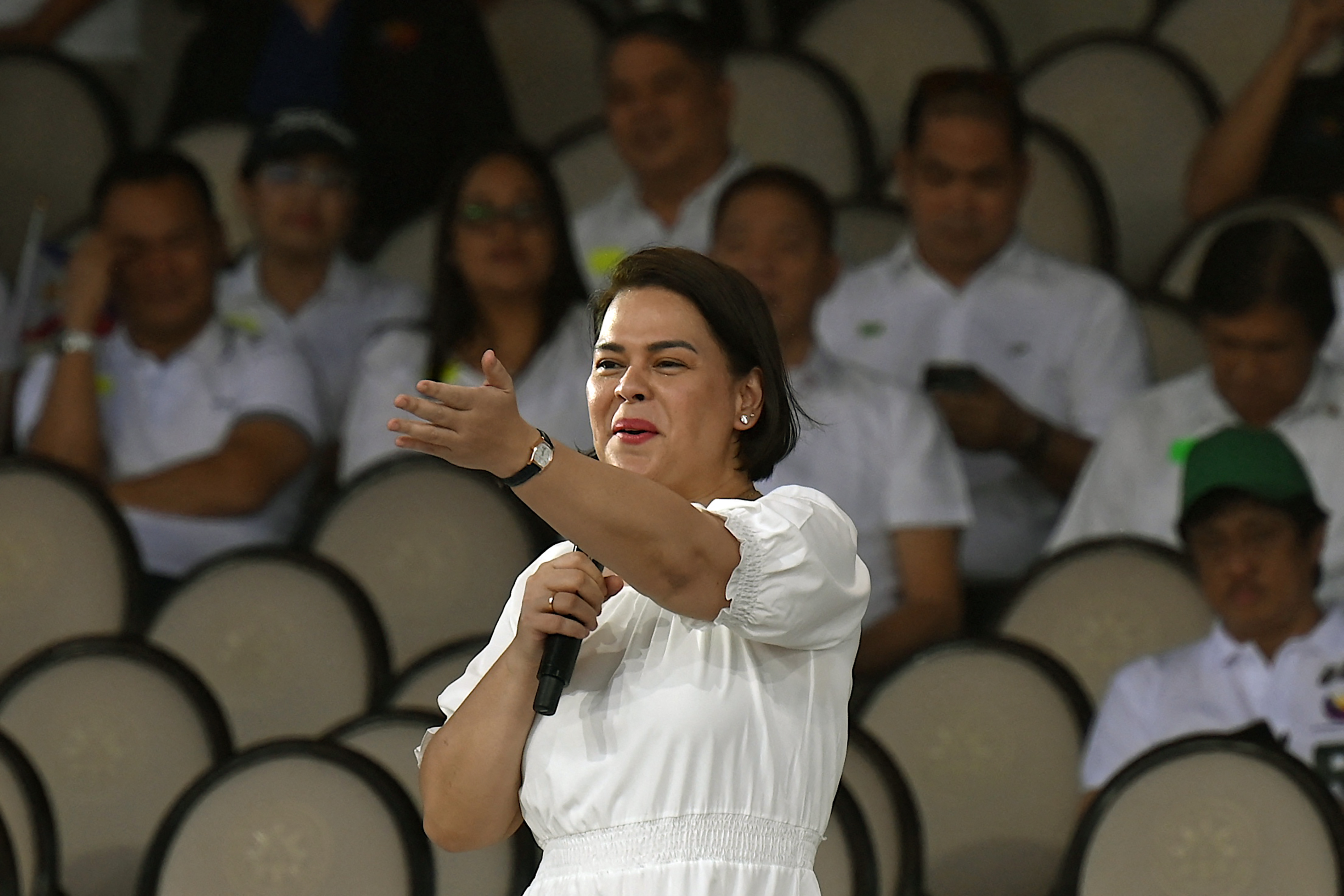 Sara Duterte speaking at a rally. She is holding a microphone. Her arm is outstretched.