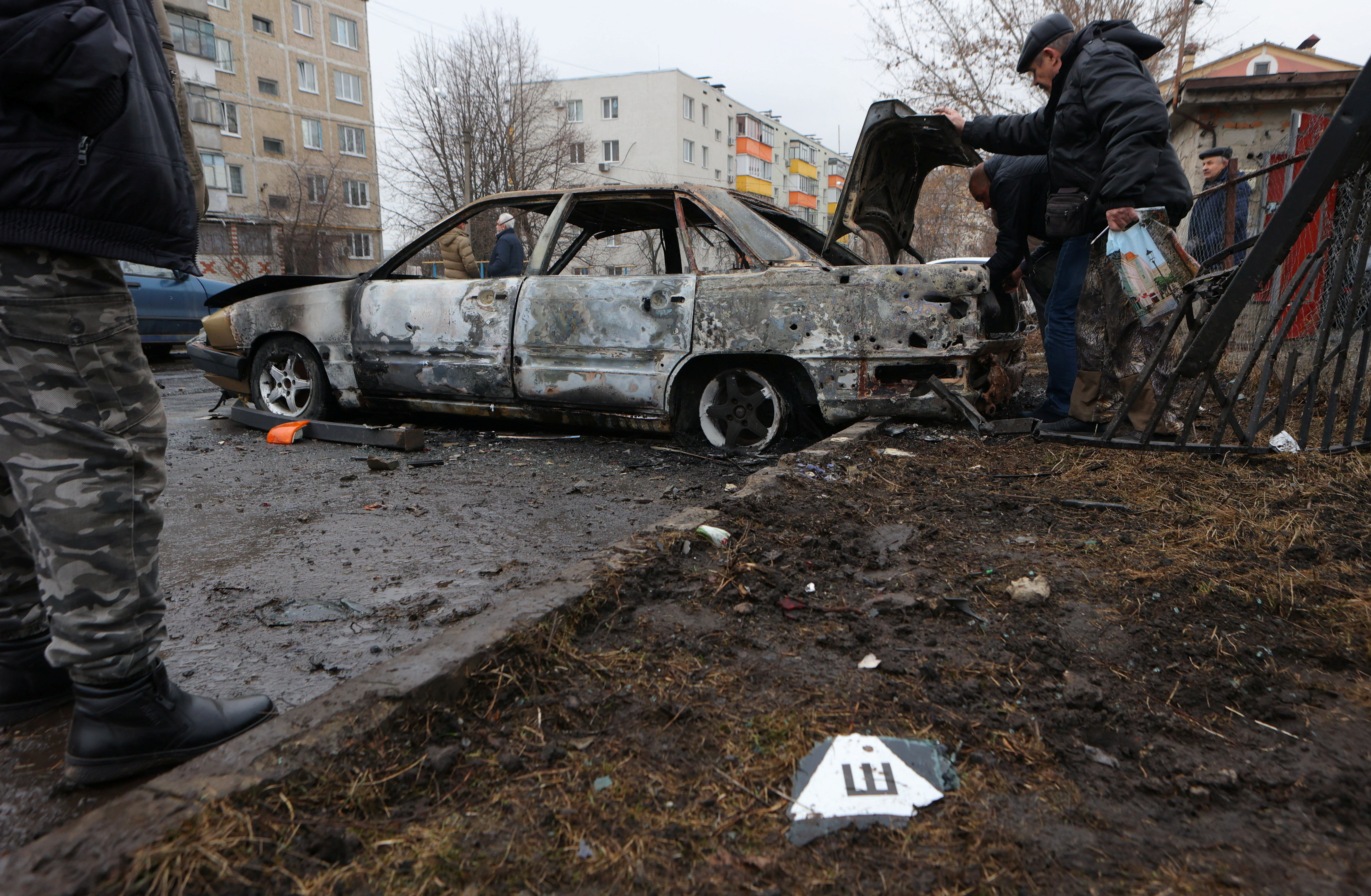 Local residents inspect a damaged car hit by shelling in the settlement of Razumnoe in the Belgorod region of Russia, March 19, 2024