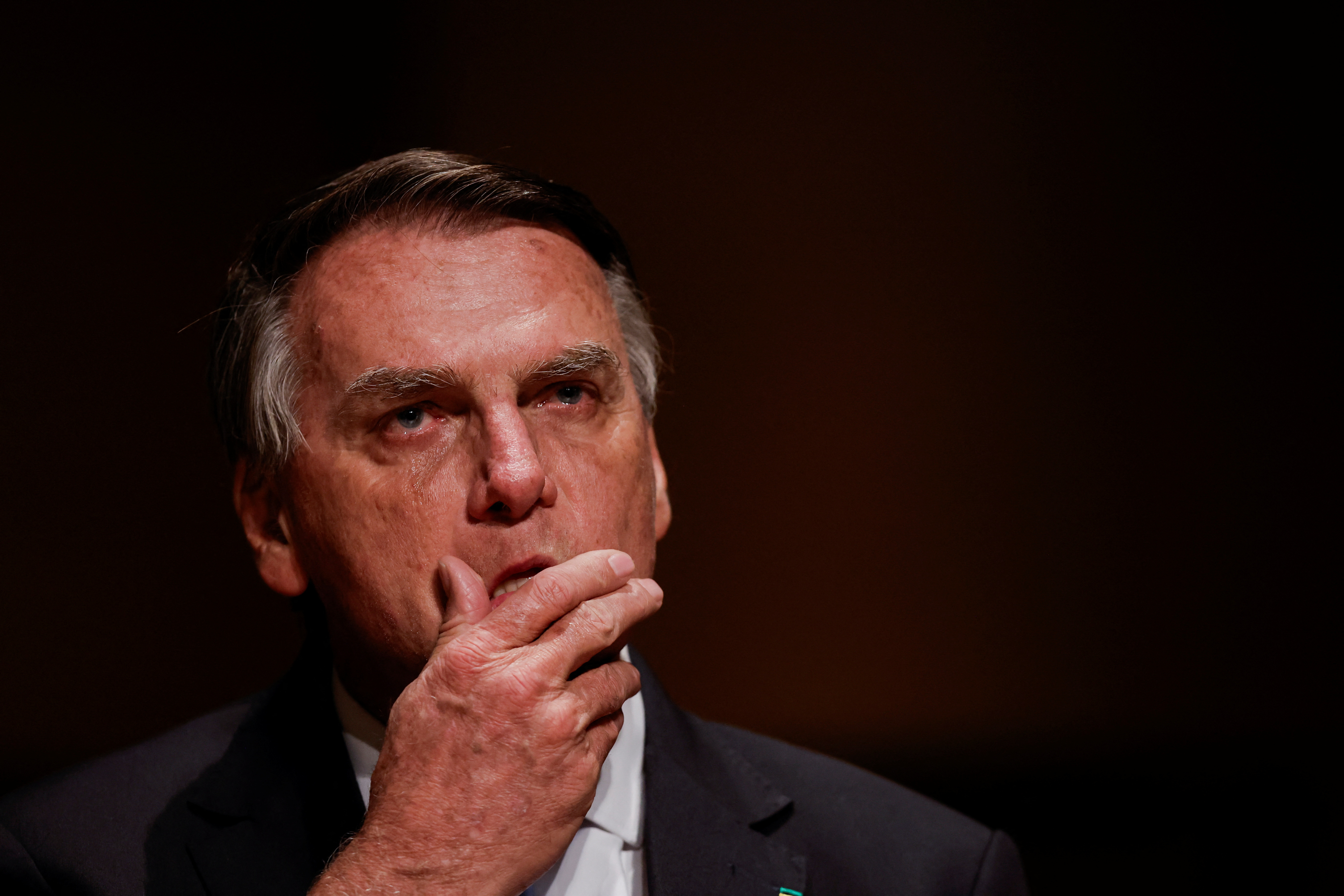 Jair Bolsonaro holds a hand to his face.