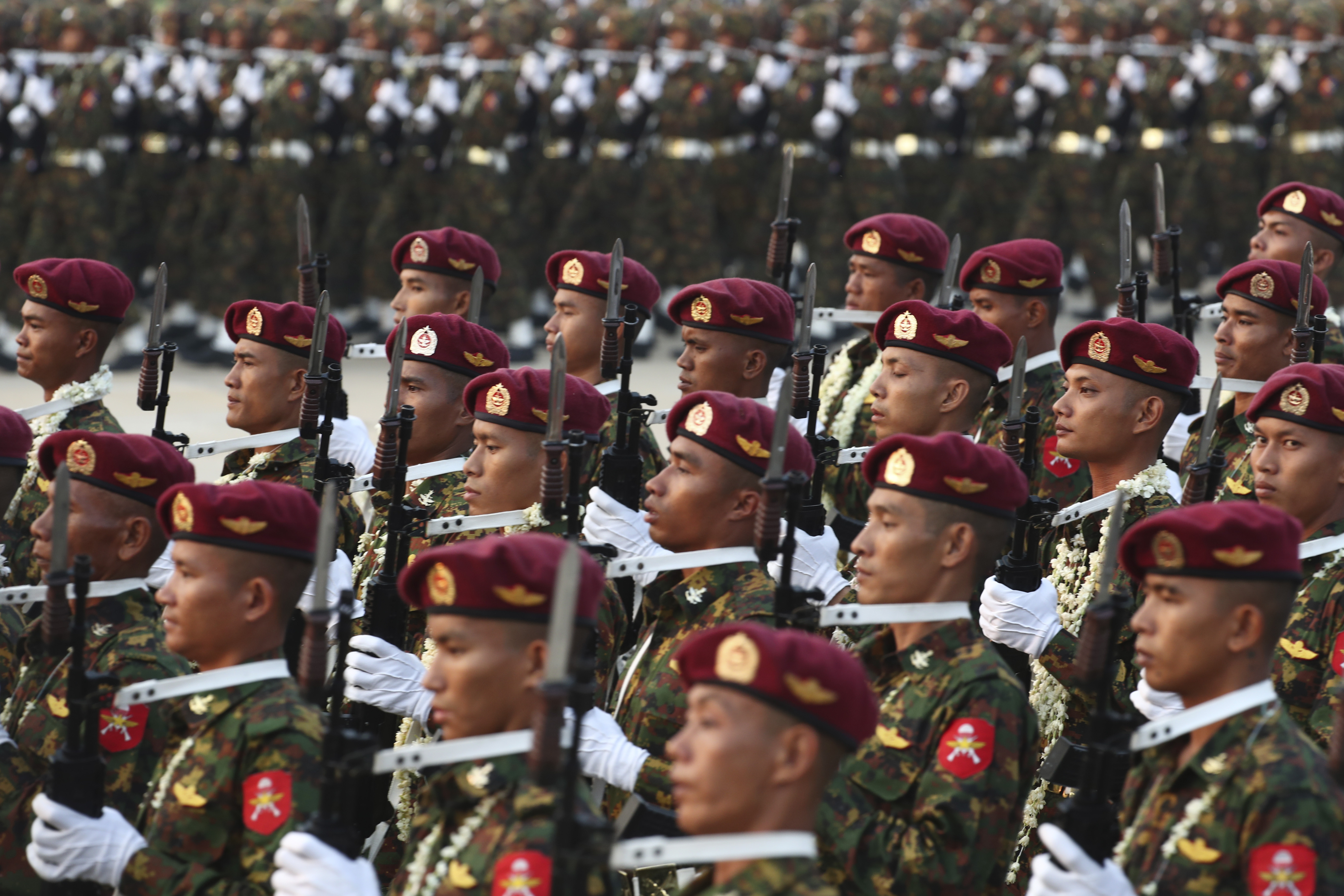 Myanmar military officers marching in formation for Armed Forces Day. They are wearing burgundy-coloured berets and are holding their weapons.