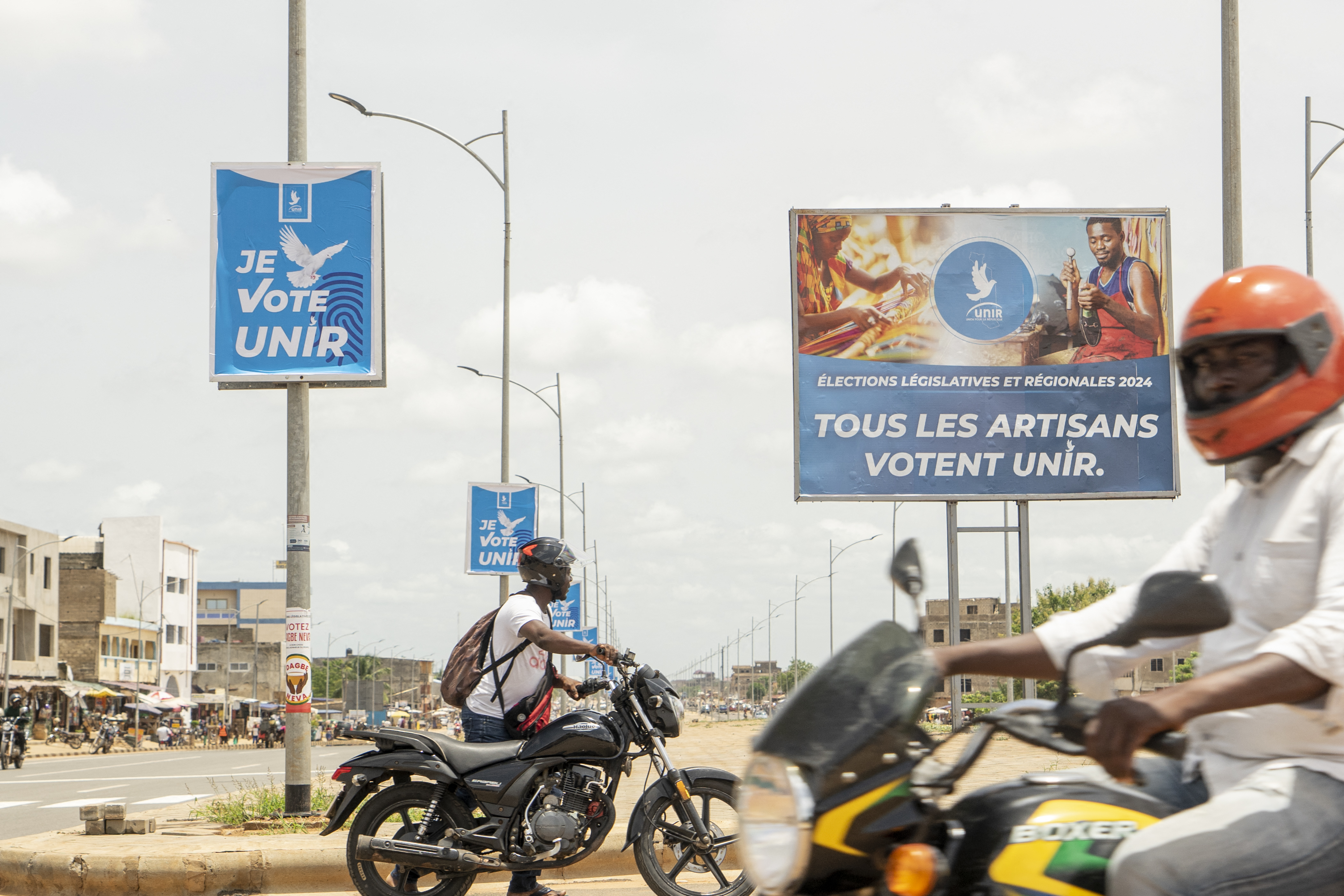 Motorbikes drive past campaign posters in Lome