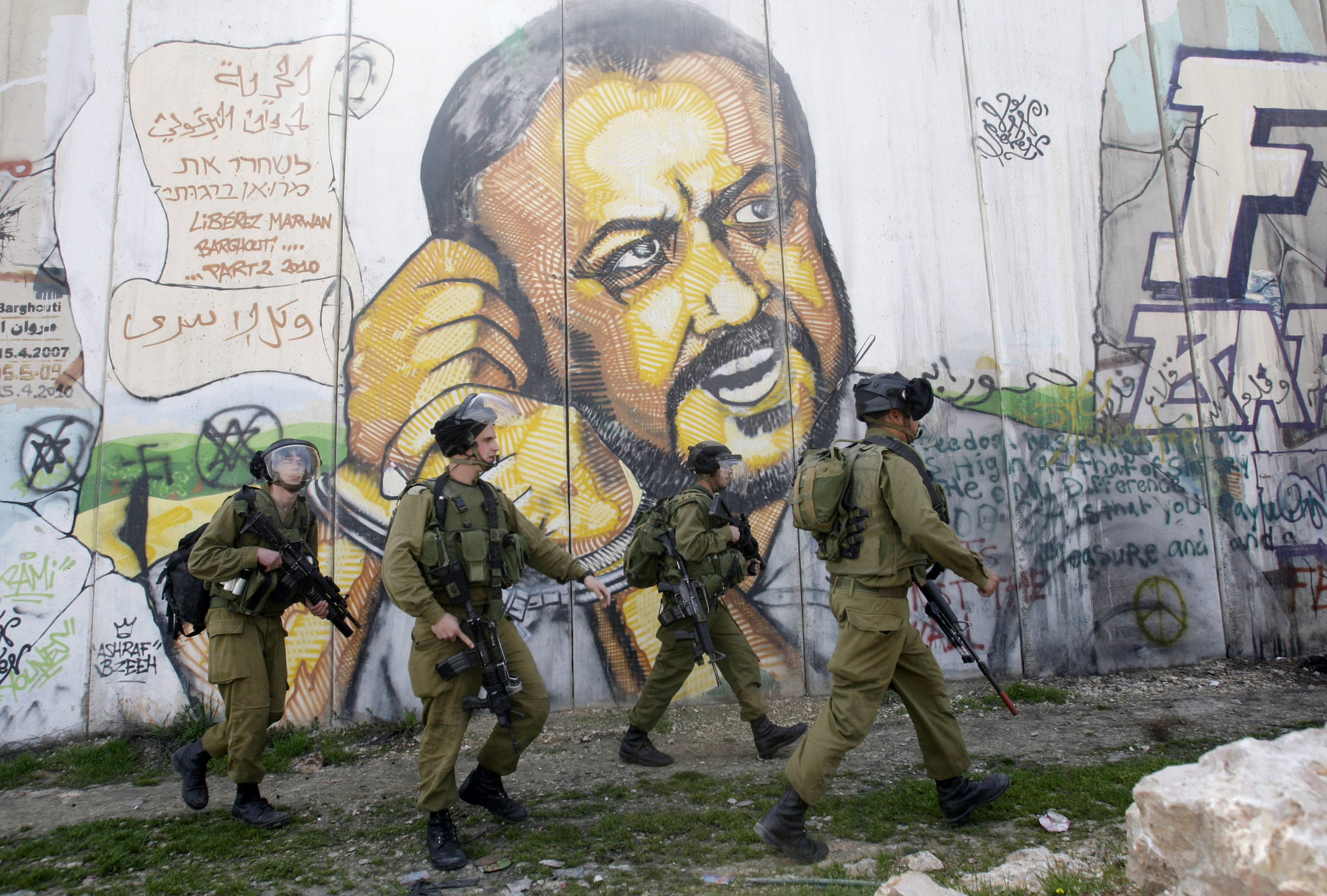 In the background of part of Israel's separation barrier with portrait of jailed Fatah leader Marwan Barghouti, Israeli soldiers patrol at Kalandia checkpoint between Jerusalem and the West Bank city of Ramallah,