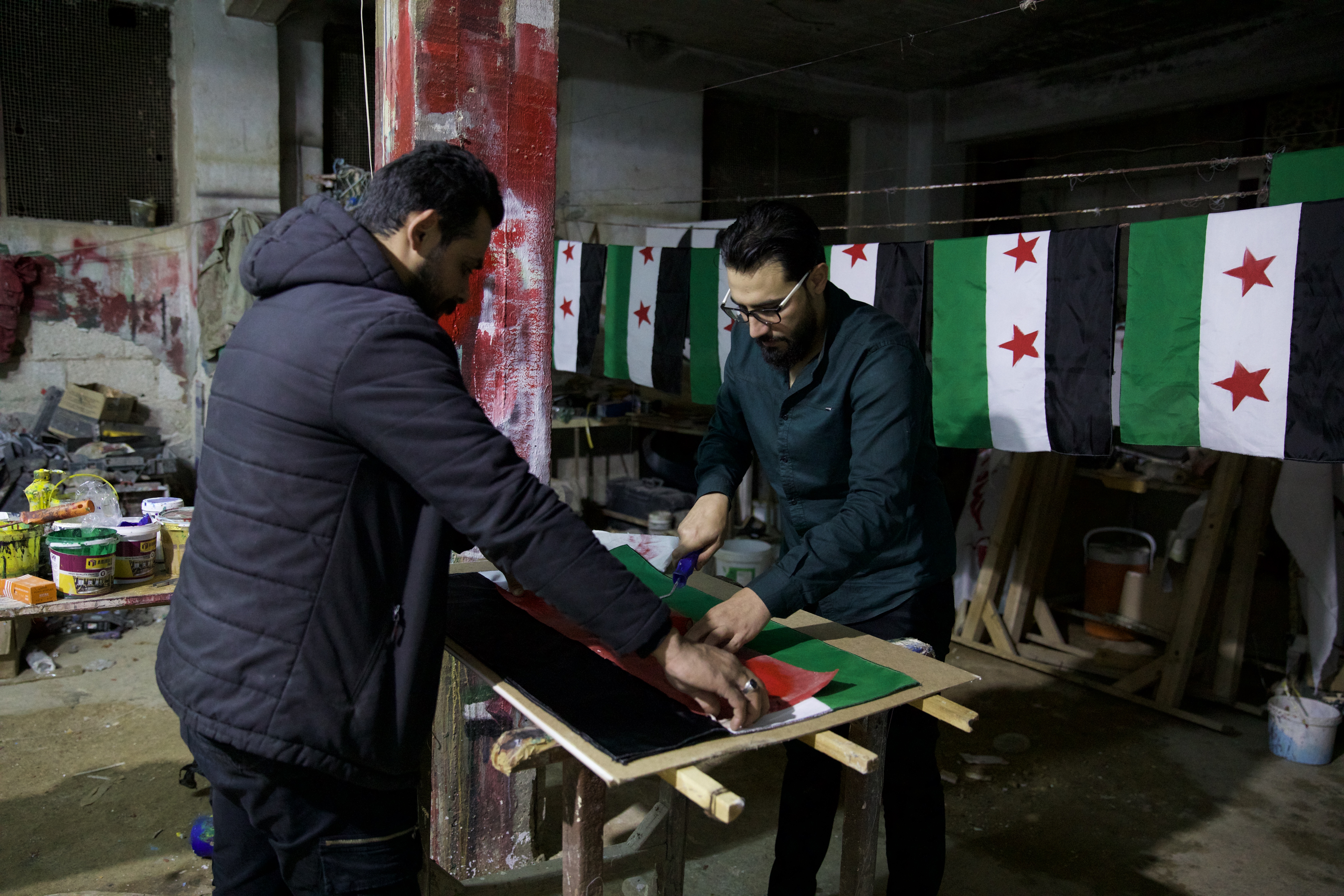 Mohammed Ali Basha, right, and a friend prepare flags for their anti-HTS protest