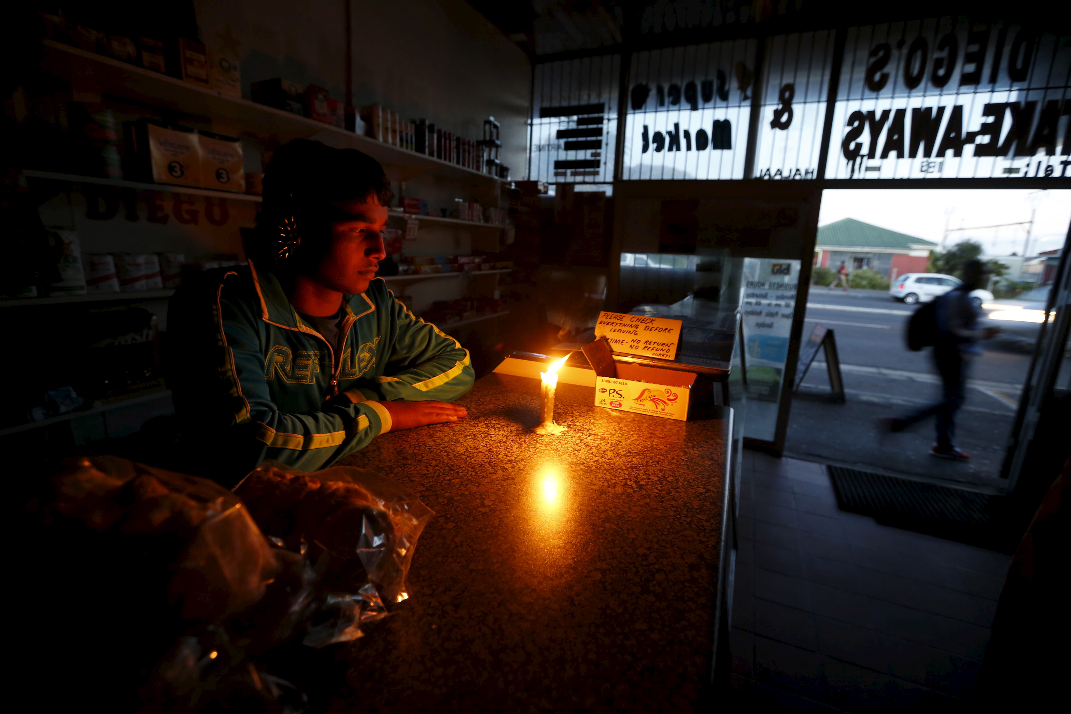 A shopkeeper waits for customers in his candlelit fast food store during a load shedding electricity blackout in Cape Town in April