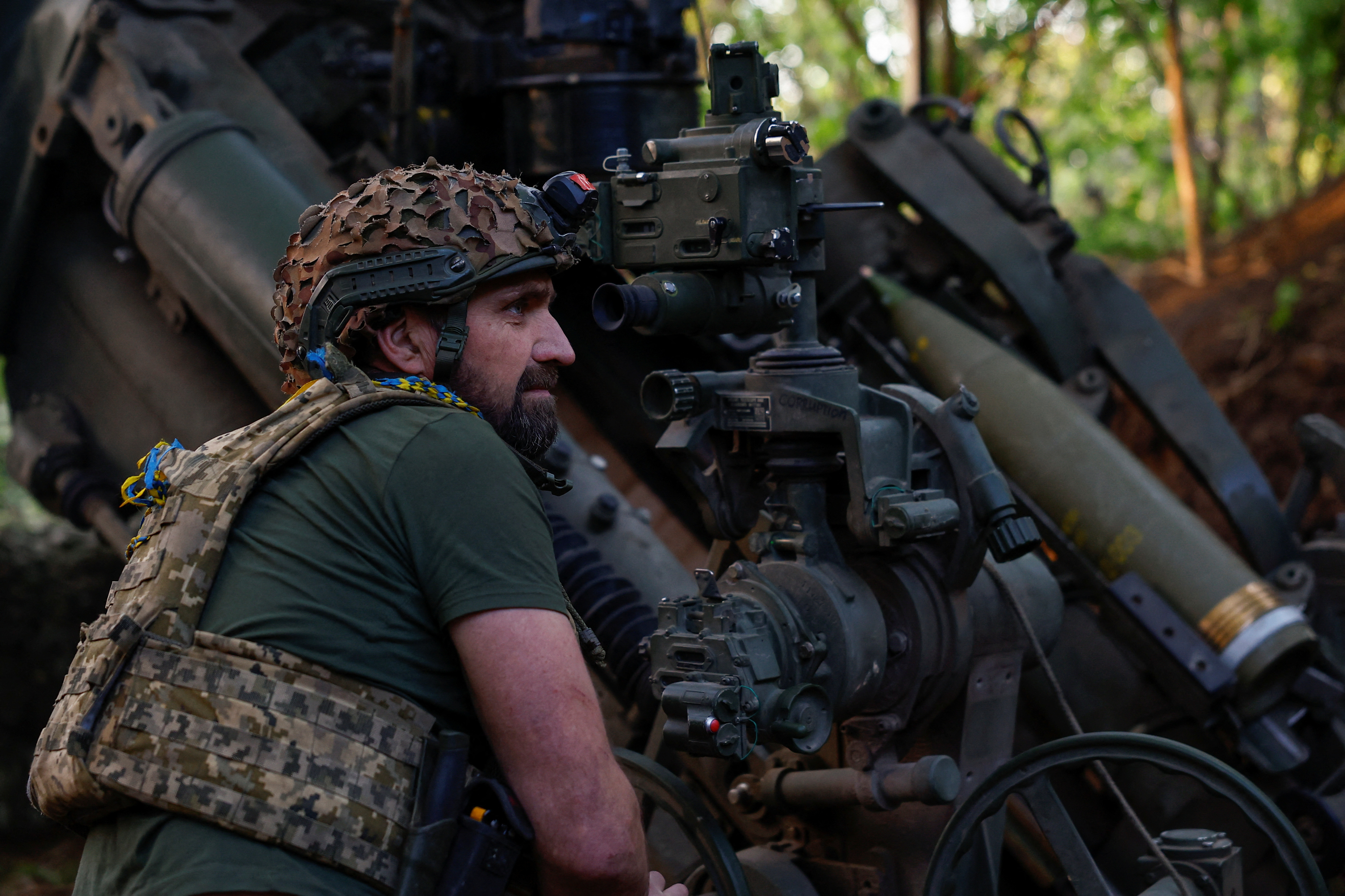 A Ukrainian soldier loading a howitzer. He is crouched alongside it.