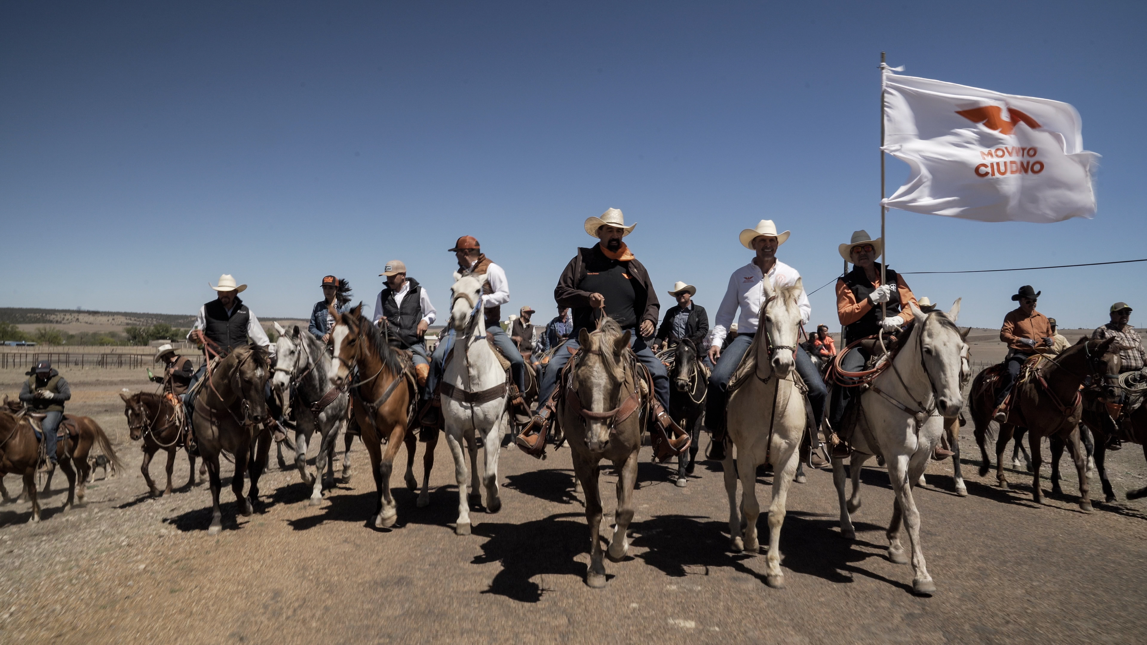 A line of political candidates and their supporters ride horses in the north Mexican desert.