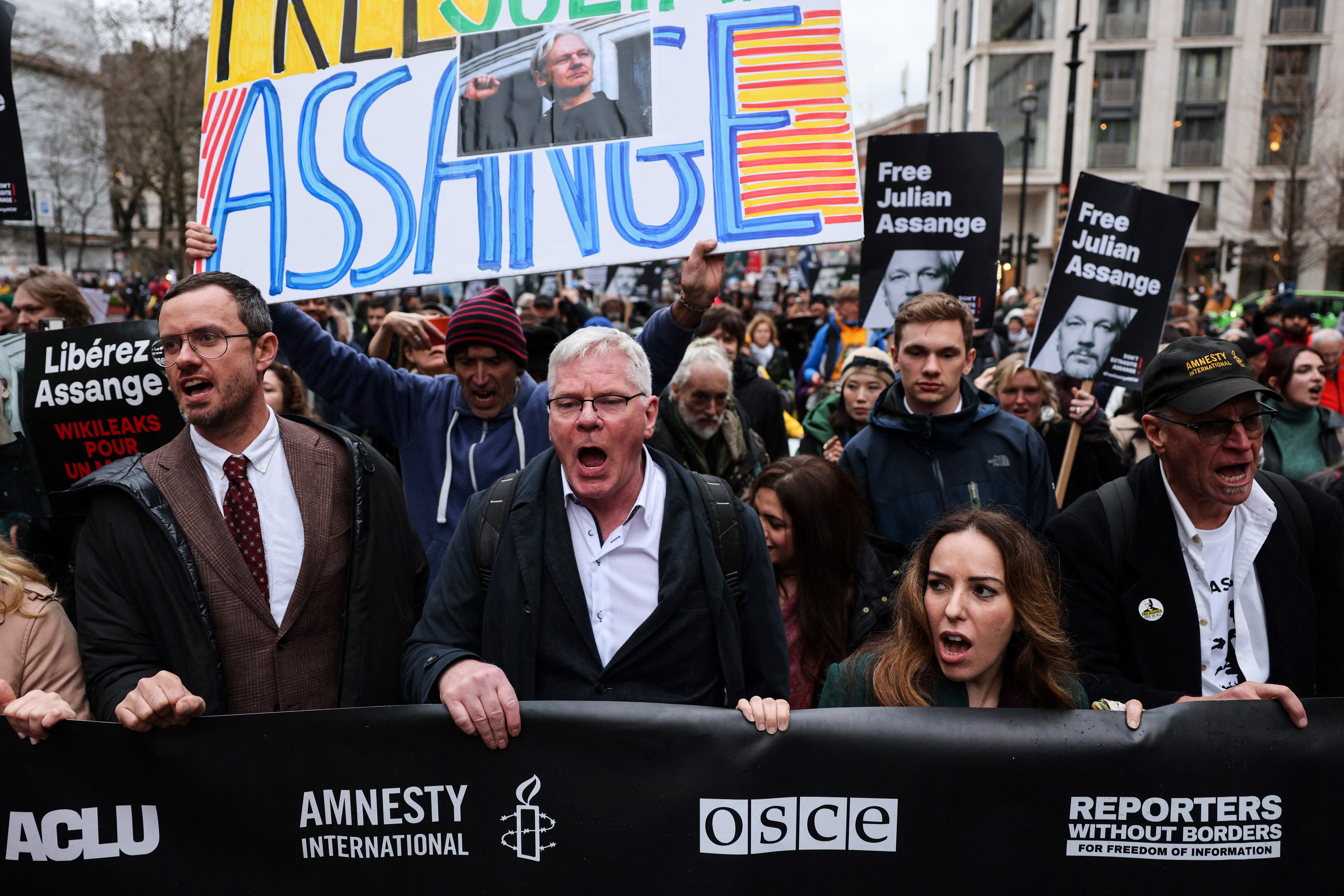 people stand in front of a sign that says free Assange