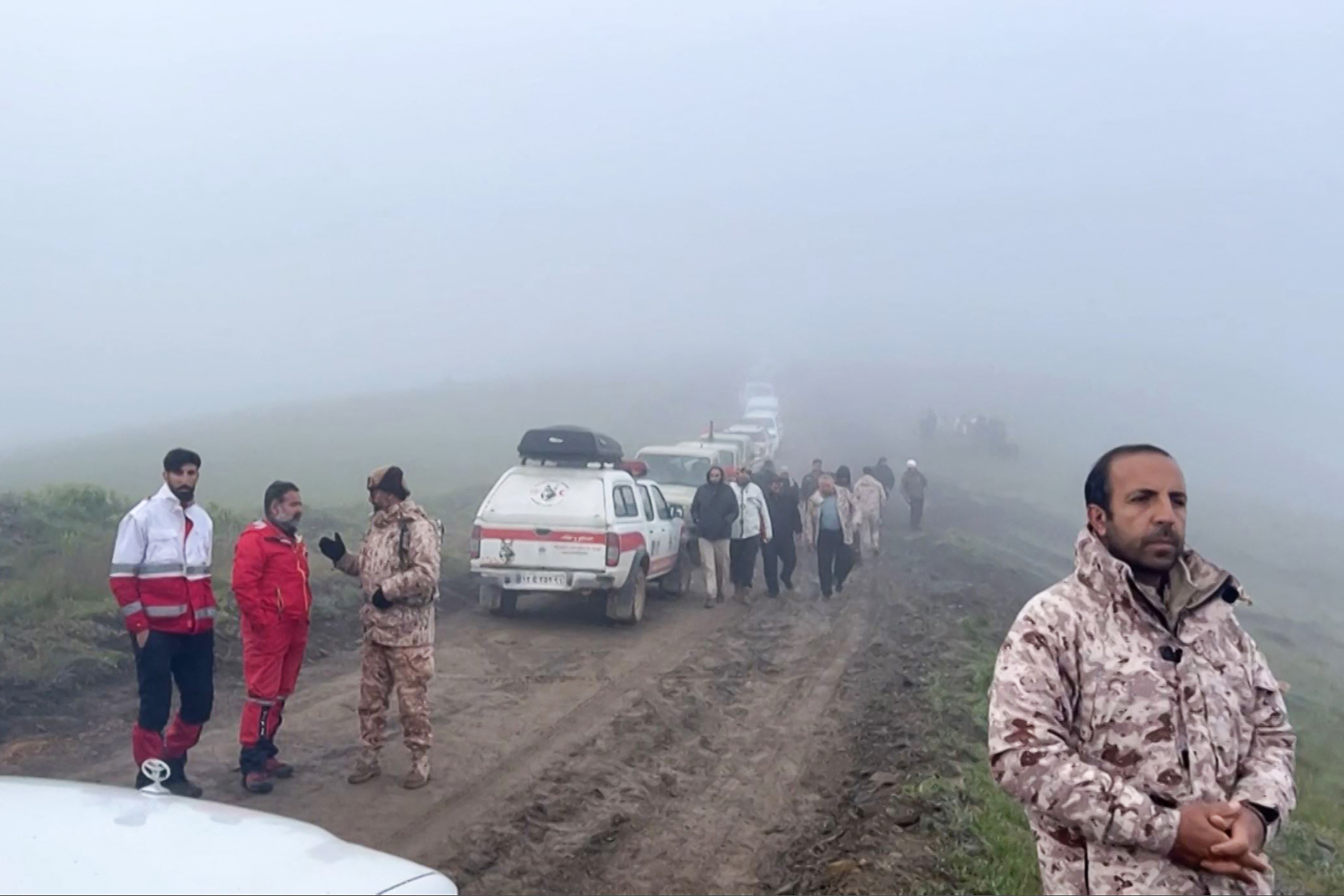 Rescue workers and their vehicles on a muddy mountain track. There is dense fog