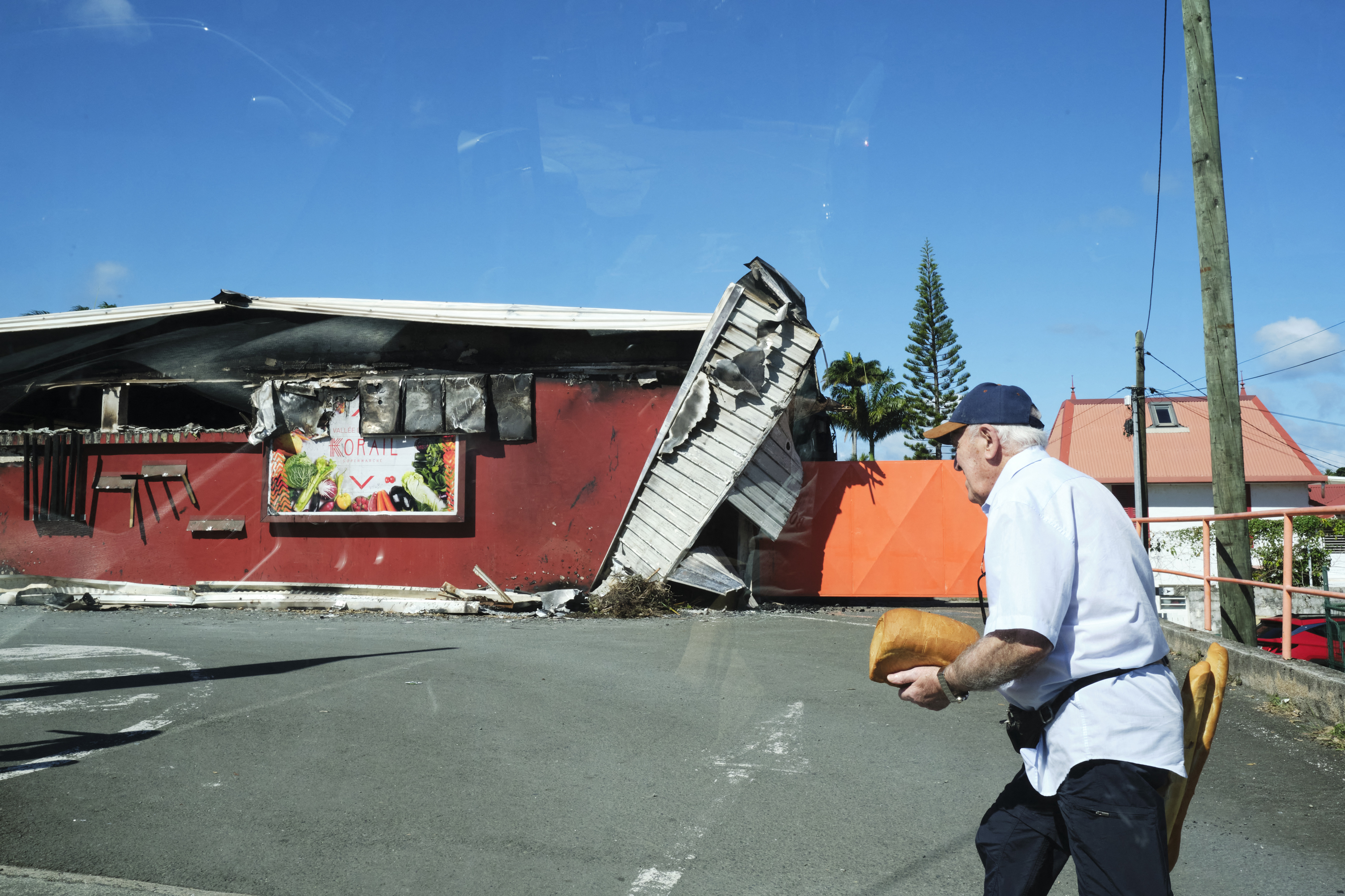 A man with a loaf of bread and two baguettes near a Noumea supermarket damaged in recent violence.