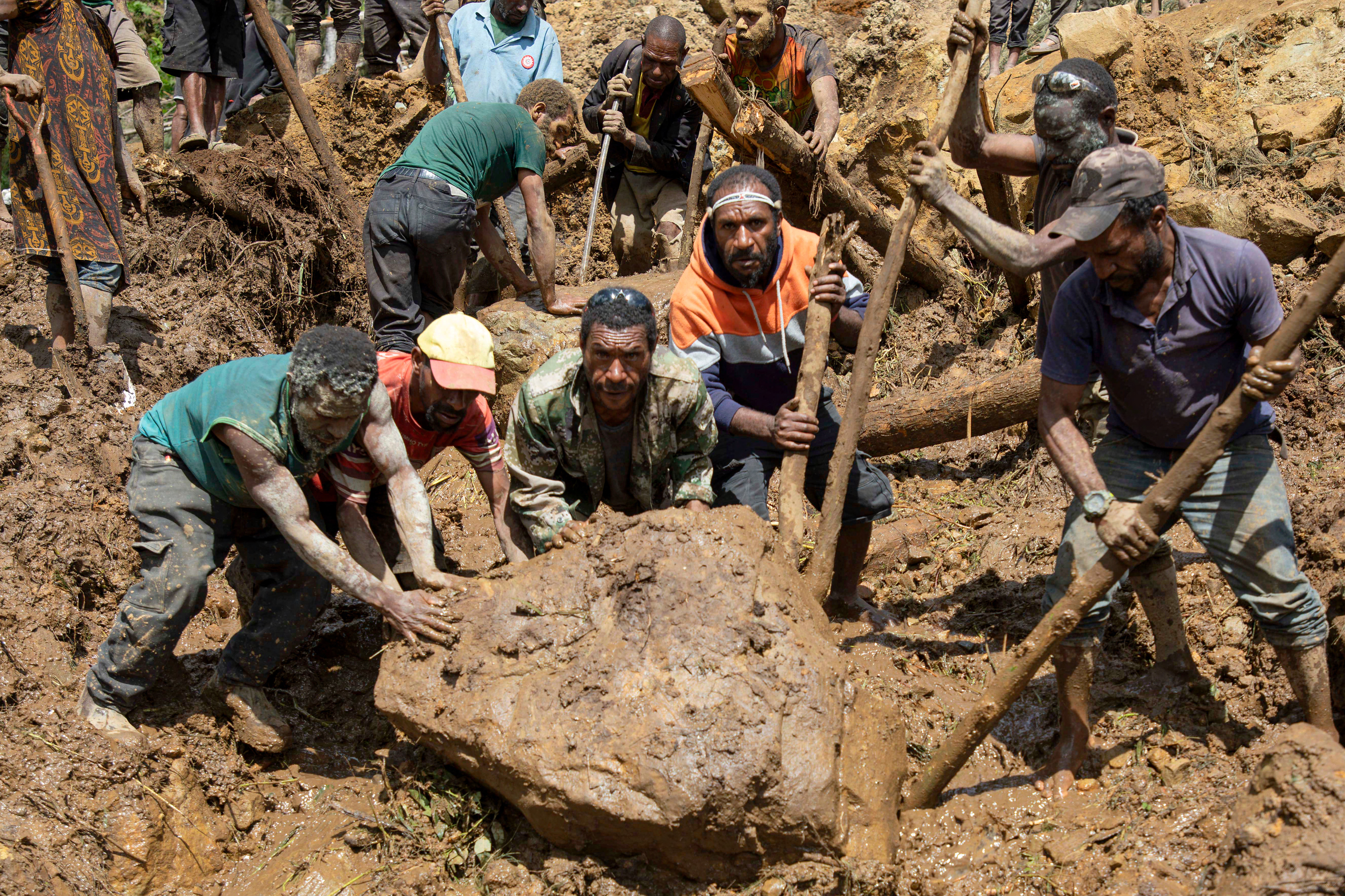 Men searching through mud and boulders with wooden sticks and their bare hands to find people buried in the landslide.