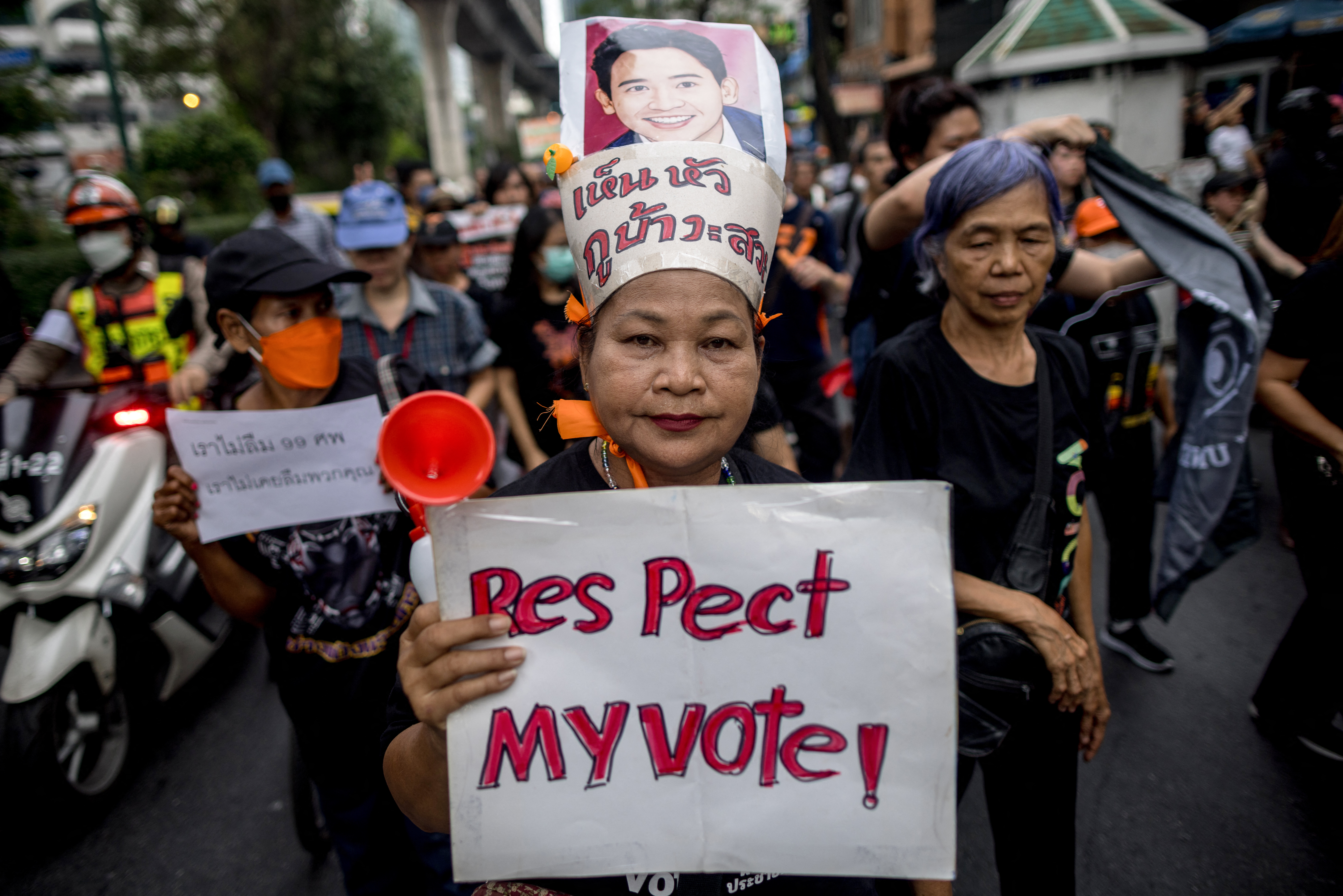 A pro-democracy protester holds a sign reading 'Respect my Vote'. Sh is wearing a headdress and lots of other people are around her.