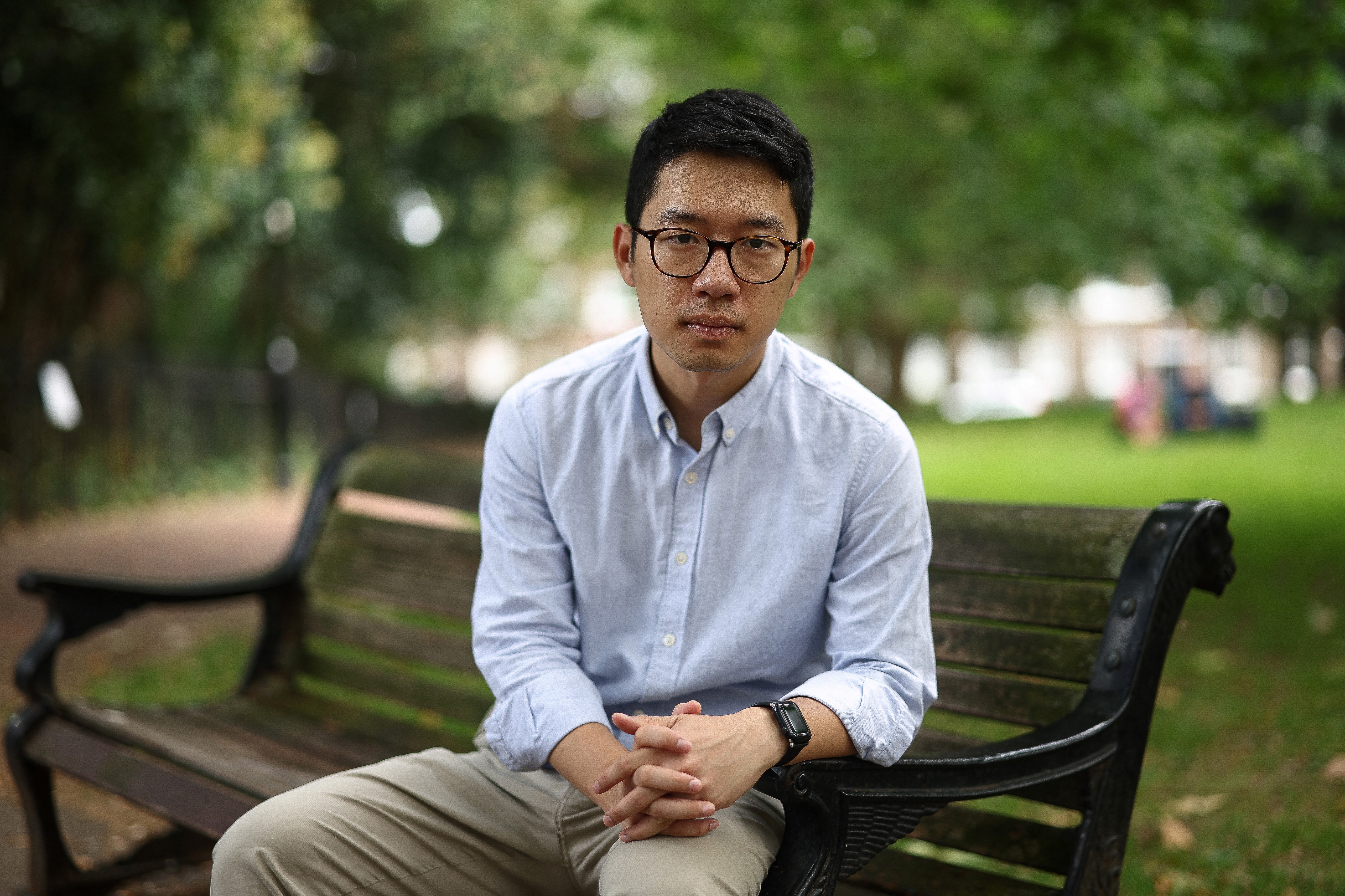 Nathan Law sitting on a bench in a London park. He looks relaxed. The park is green and leafy.