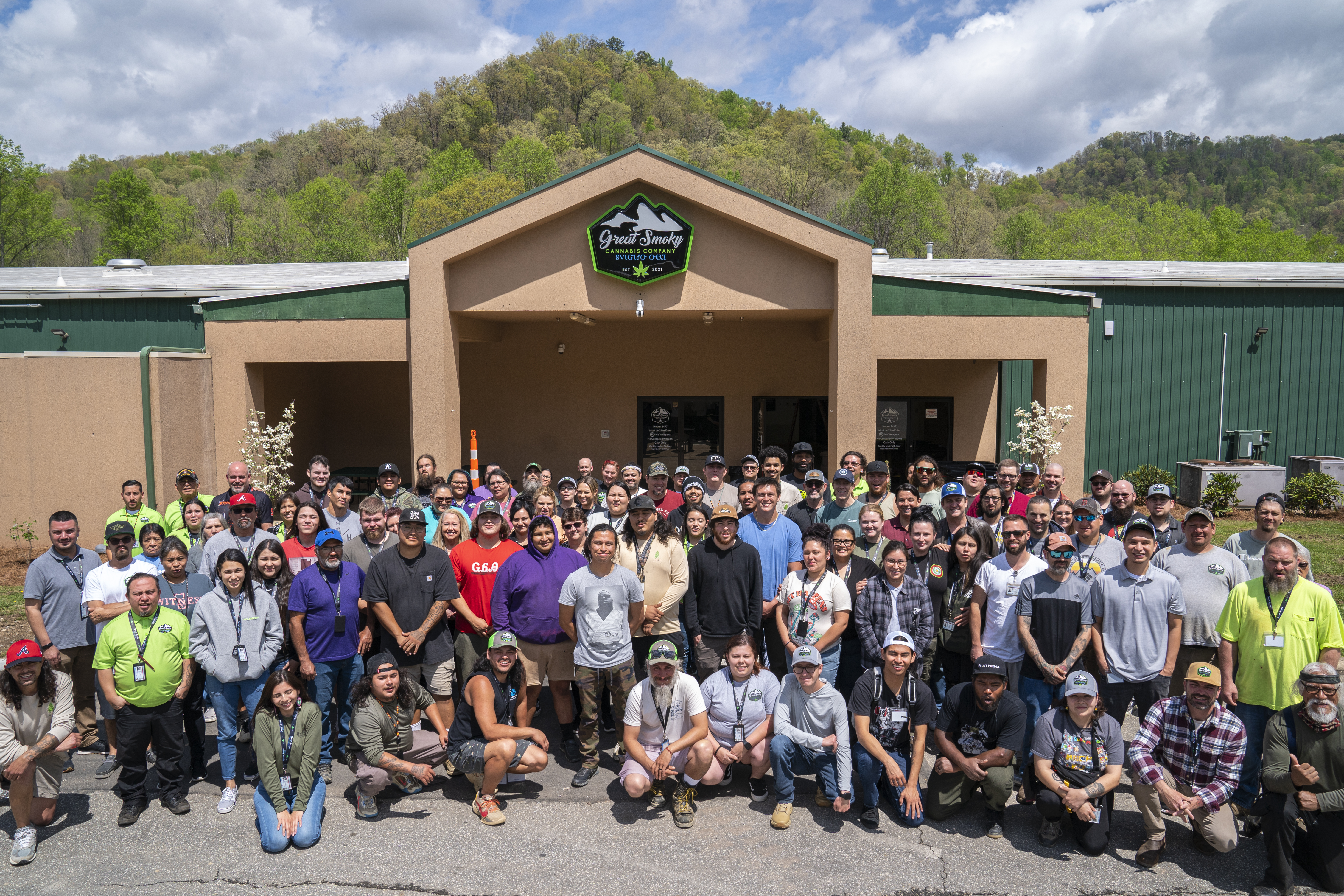 Employees and members of the Cherokee nation gather in front of the Great Smoky Cannabis Company, a brown single-story building.