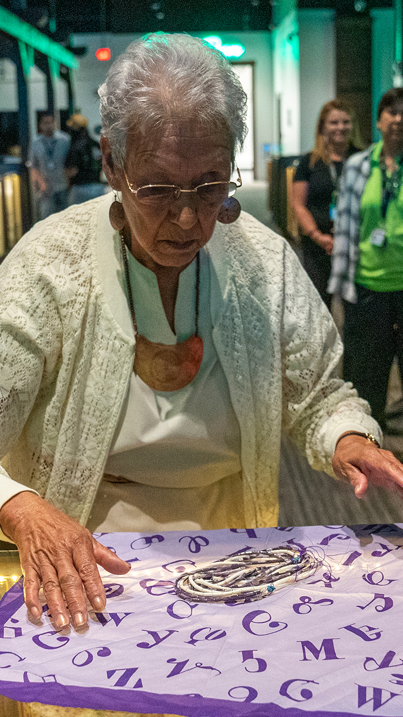 Myrtle Driver, a Beloved Woman and tribal elder, spreads out a purple handkerchief on a table, with strings of wampum beads sitting inside.