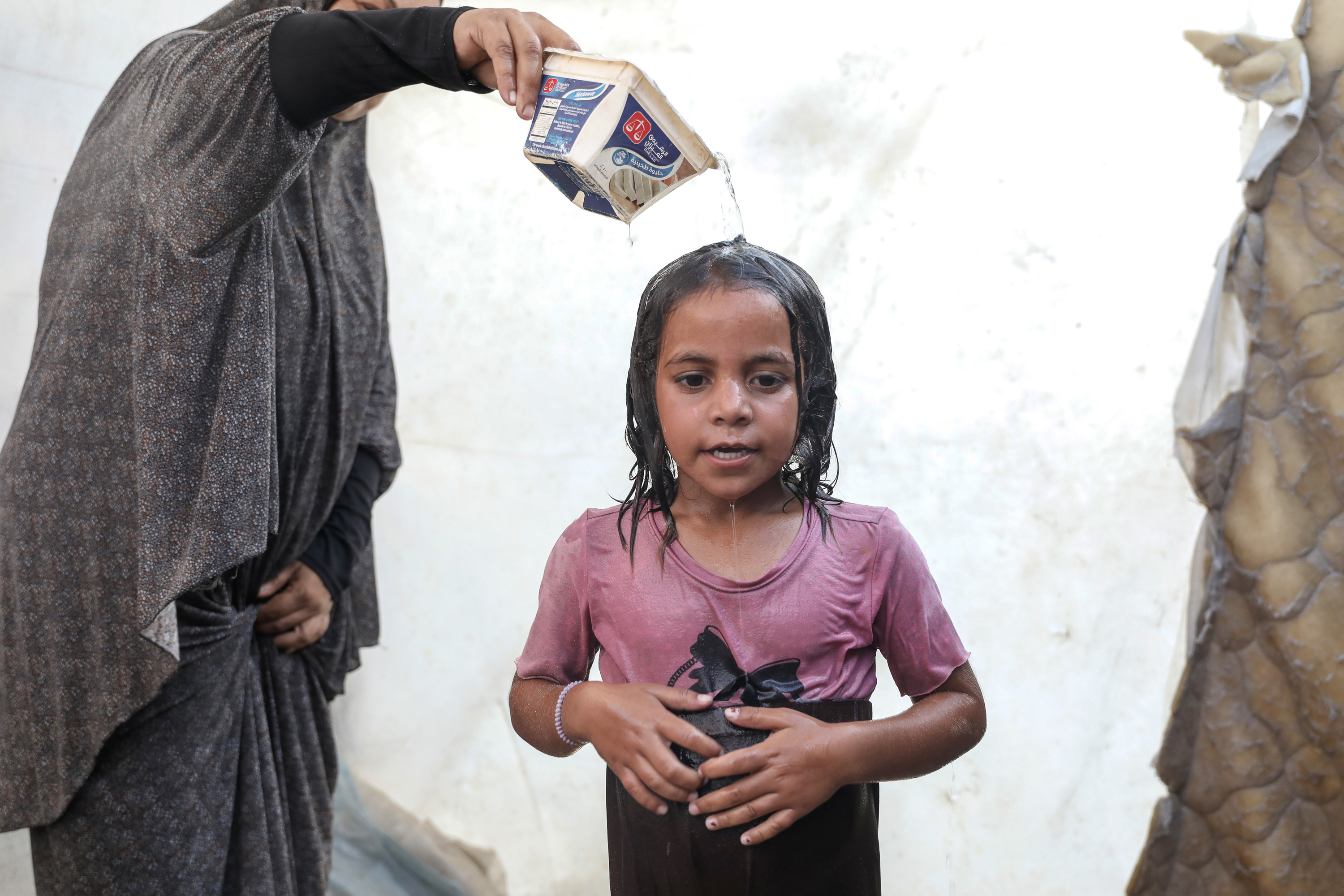 Nimah pours water over her daughter after the family escaped to the sea for the day